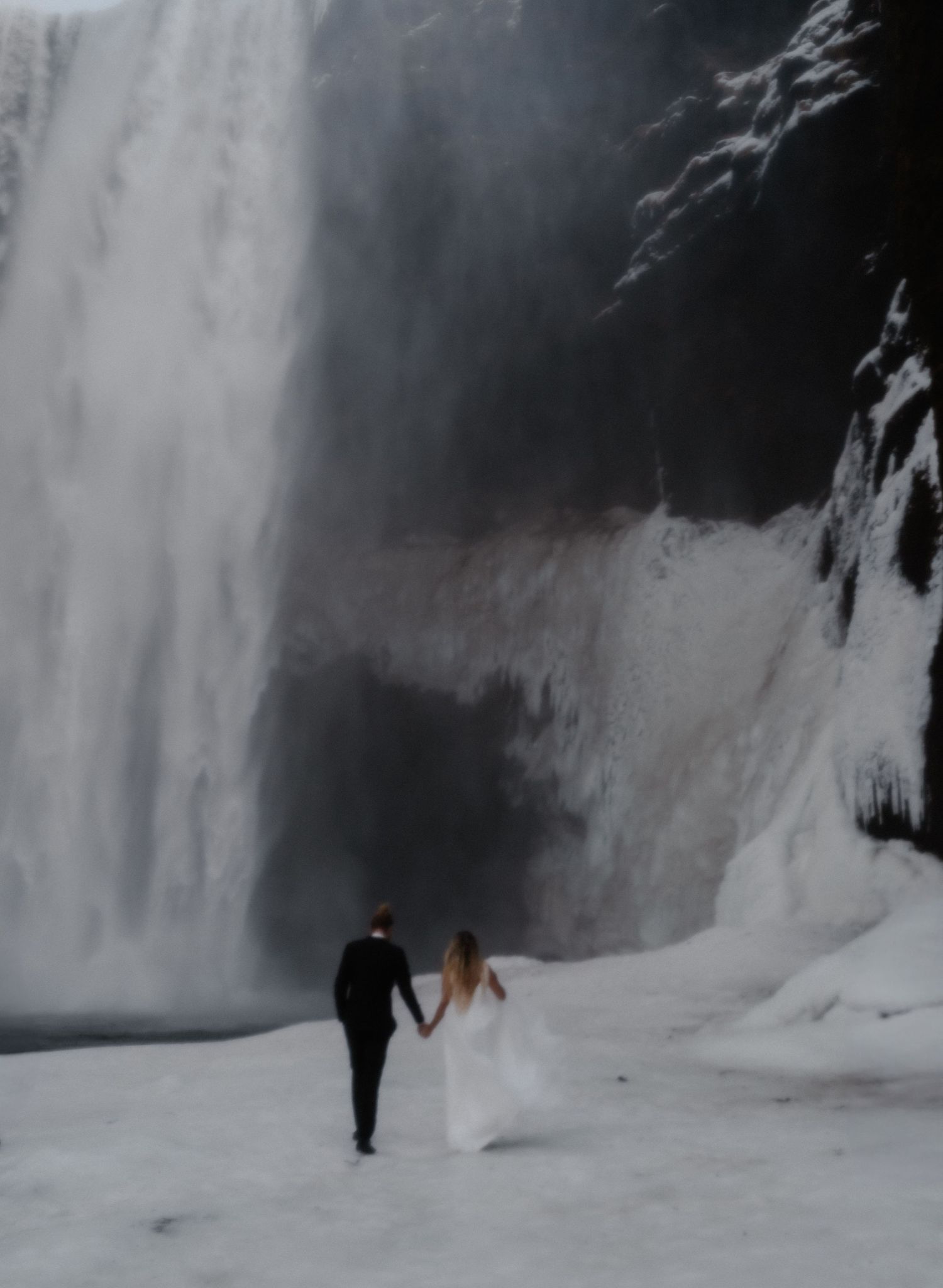 A person walks through a snowy landscape with frozen waterfalls and ice formations in the background.
