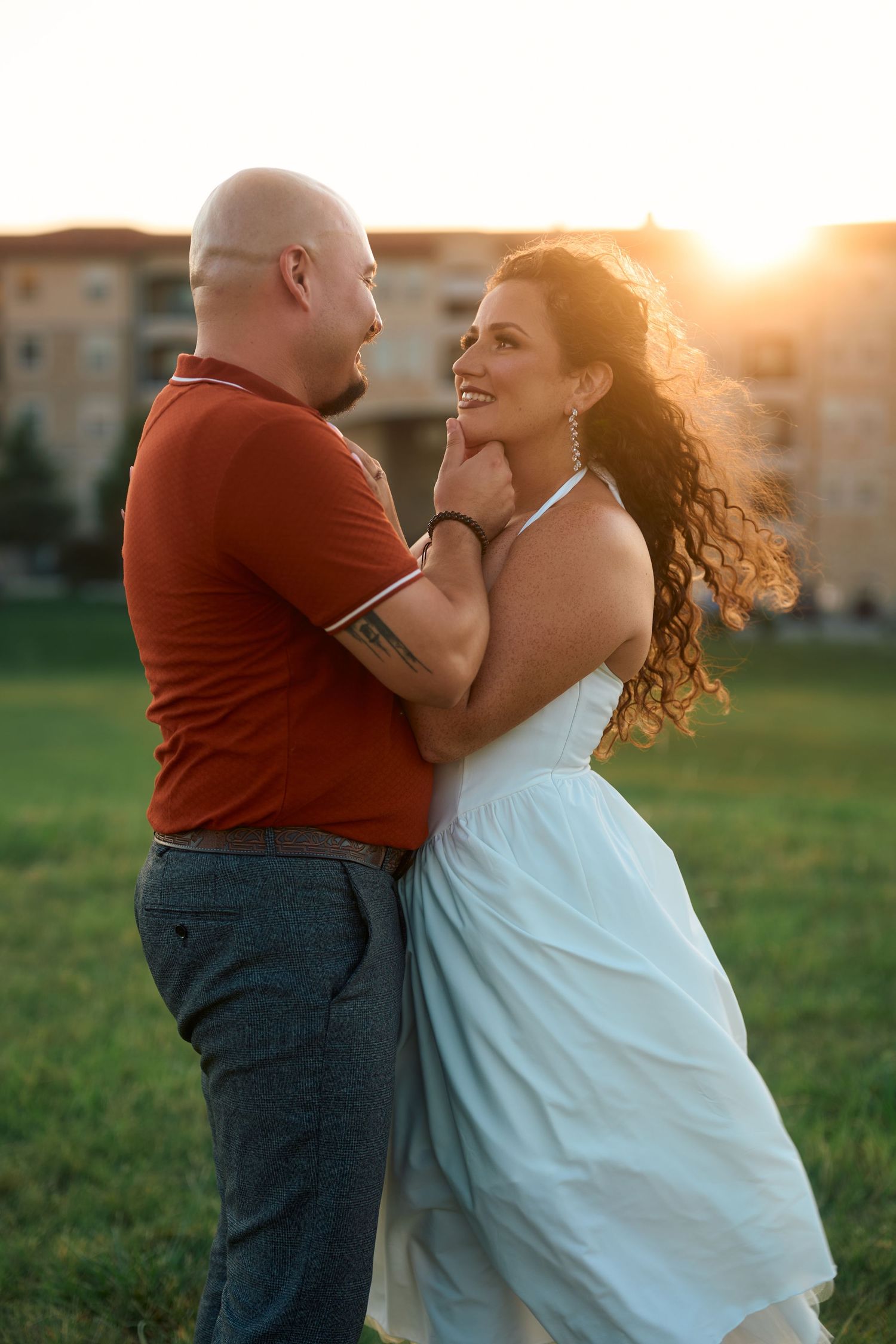 Couple in romantic embrace during golden hour in grassy field.