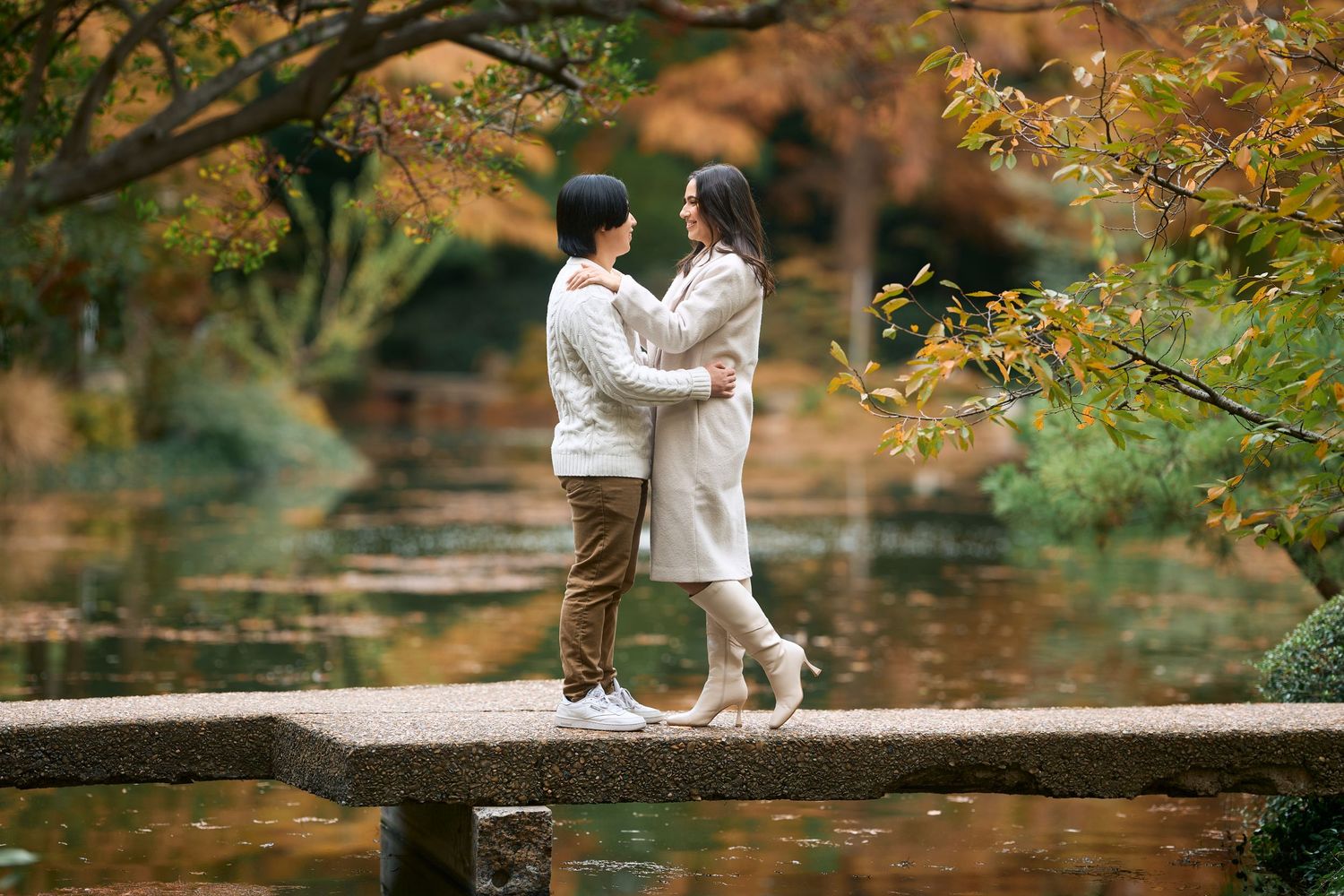 Couple embraces romantically in a park during autumn with golden leaves in the background.
