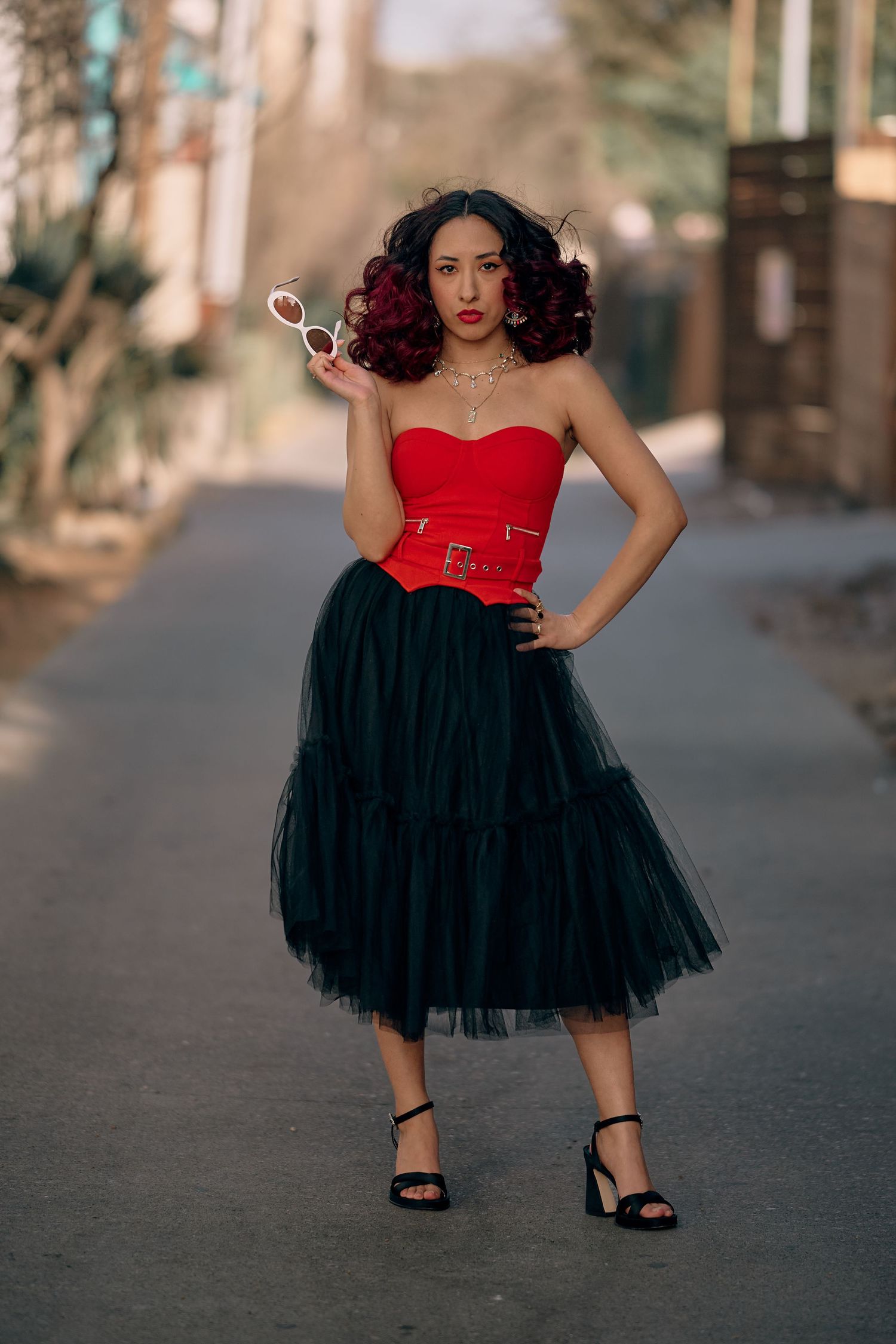 A vintage-inspired outfit featuring a red strapless corset top and black tulle midi skirt on a city street.