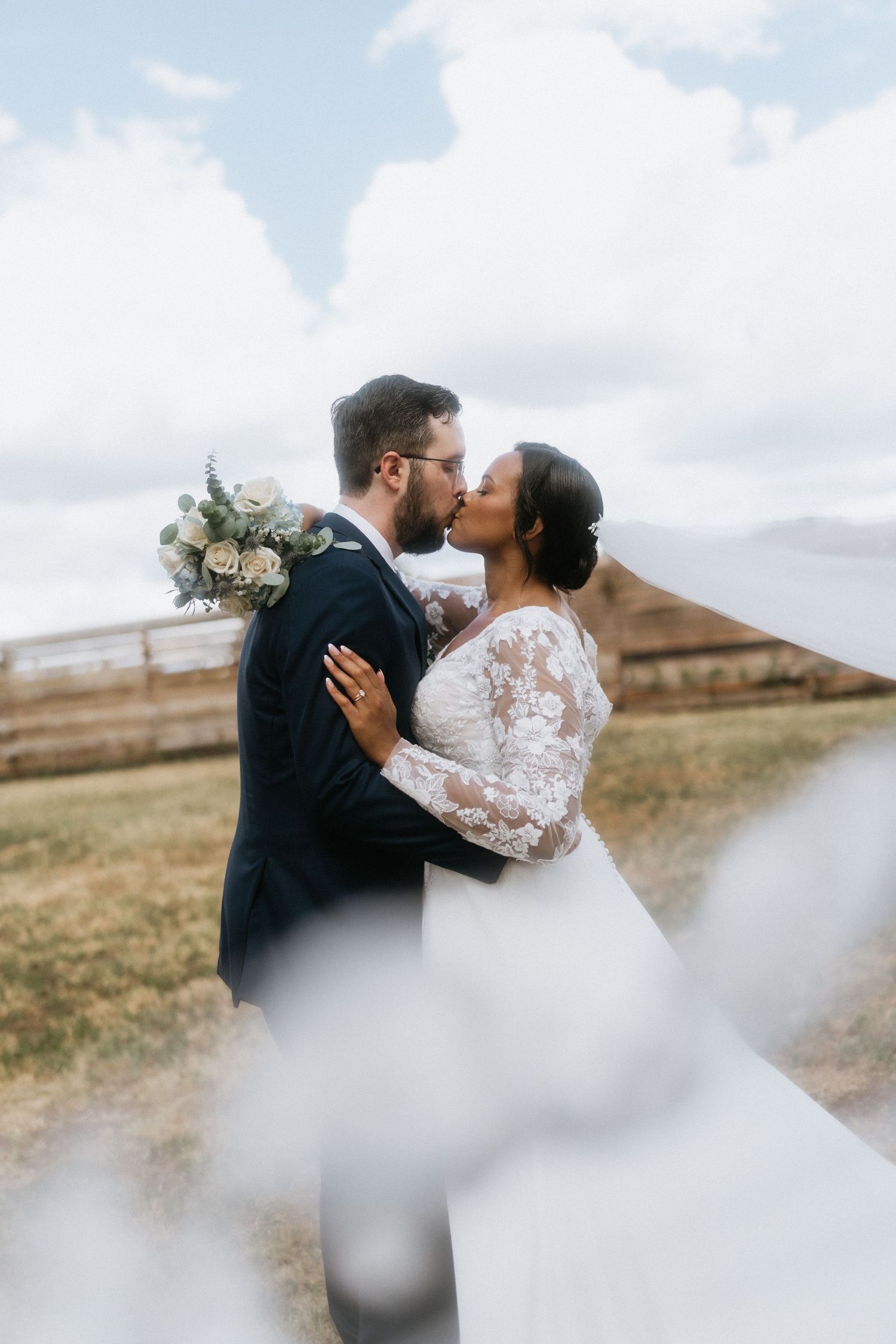 Wedding couple embracing in an outdoor setting with cloudy sky backdrop.