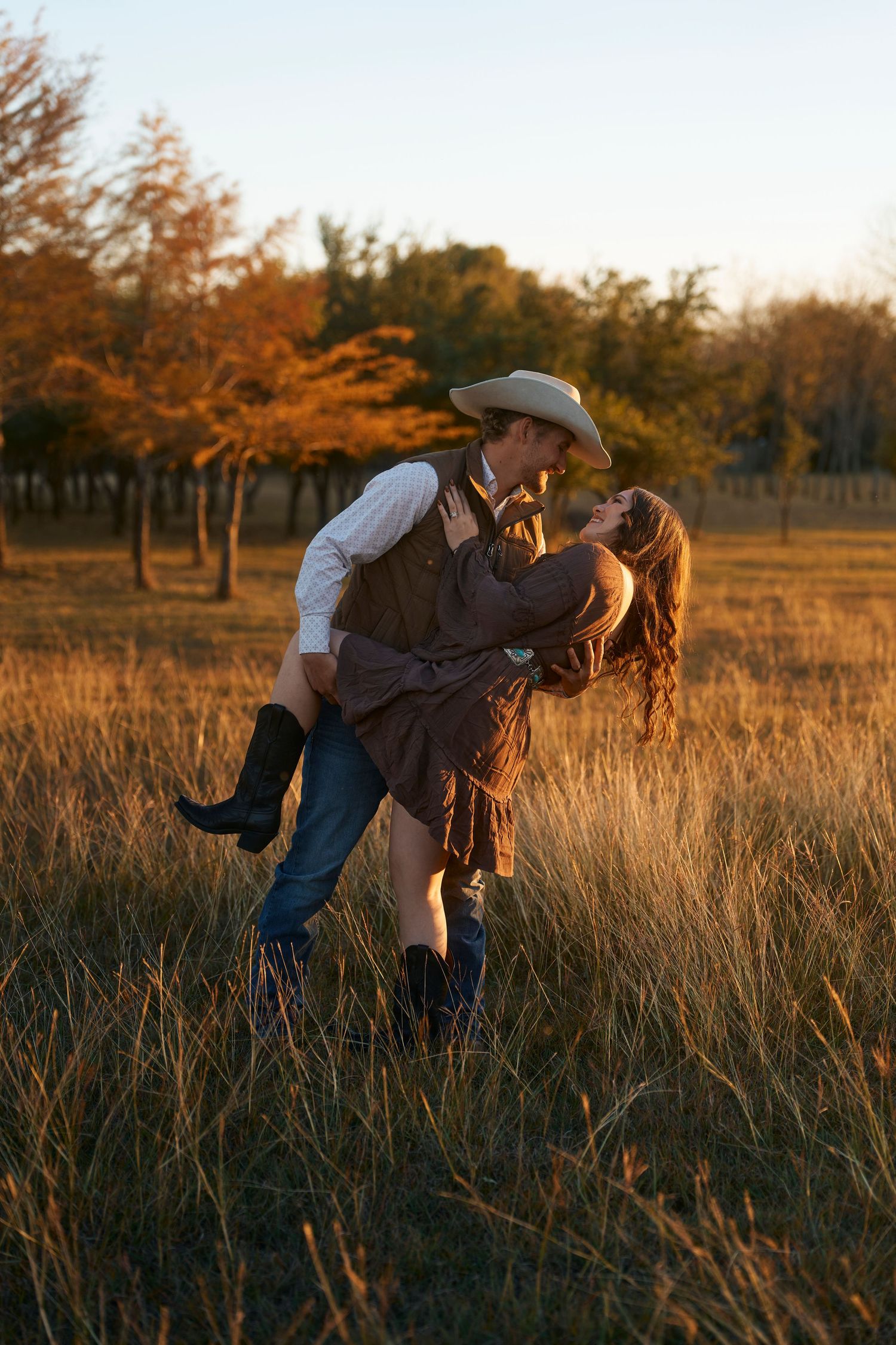 Romantic couple in western attire share intimate moment in golden autumn field at sunset.