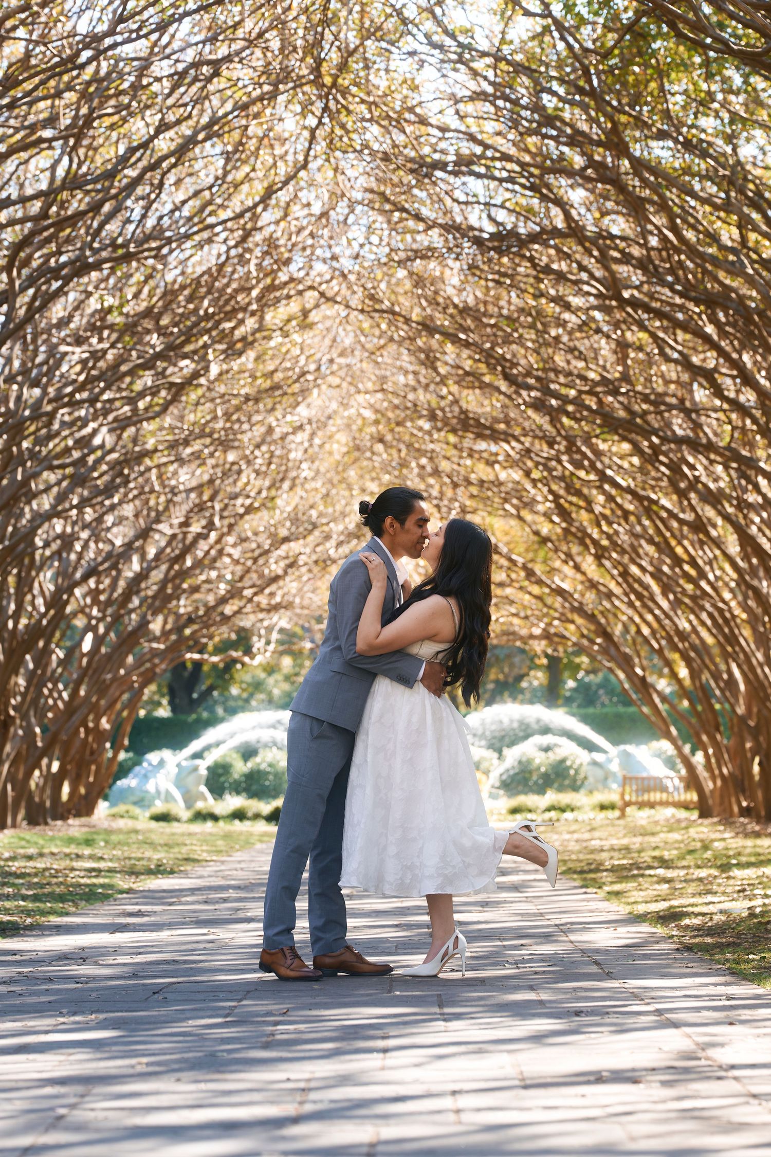 Couple sharing a romantic kiss under a canopy of golden trees on a scenic pathway during an outdoor engagement session.