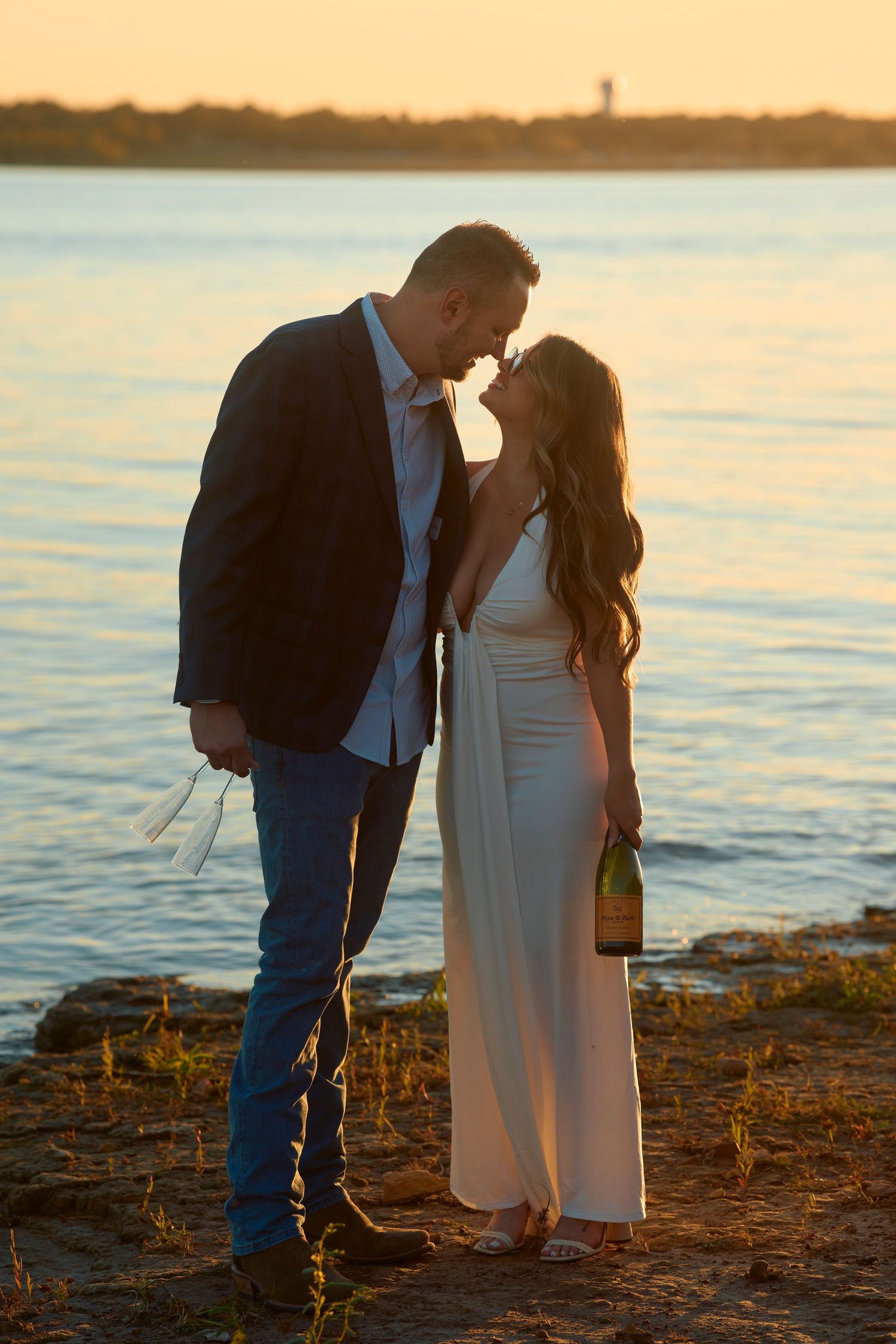 A romantic sunset silhouette shows a couple embracing on the shoreline during golden hour.