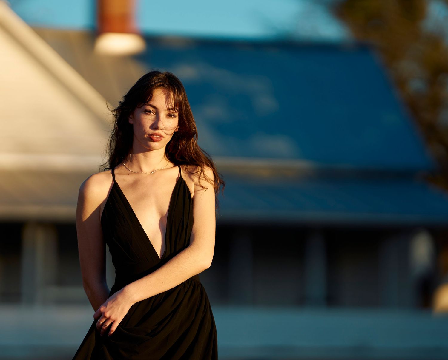 A person in a black dress poses gracefully against a blurred outdoor background at sunset.