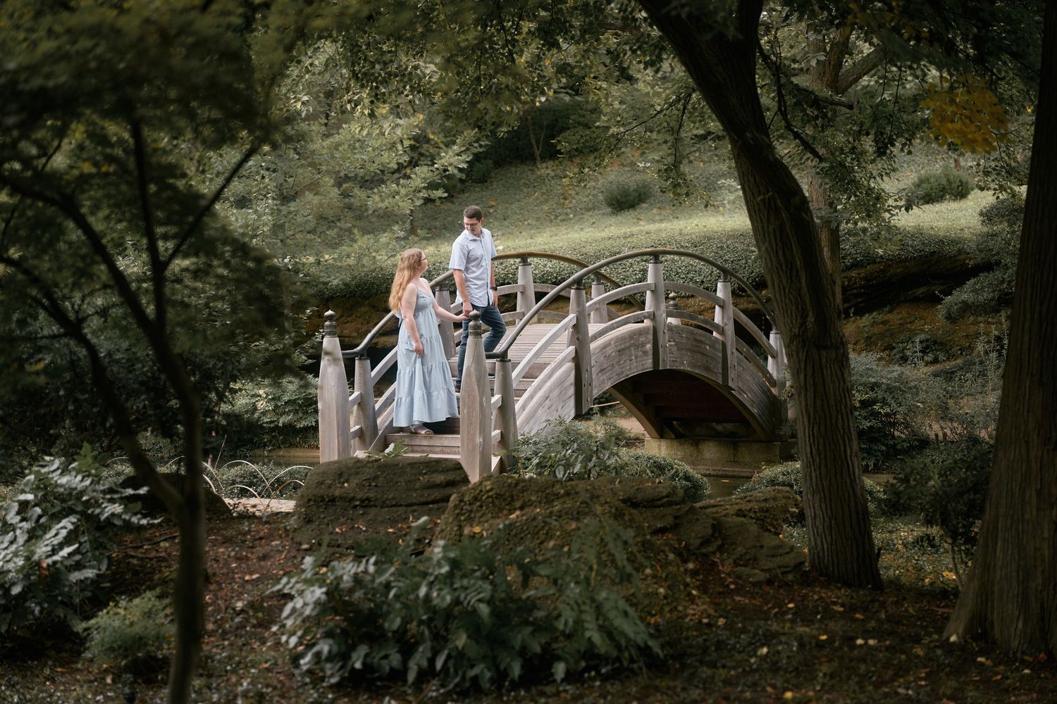 Couple walking through wooded path holding hands during outdoor photoshoot.