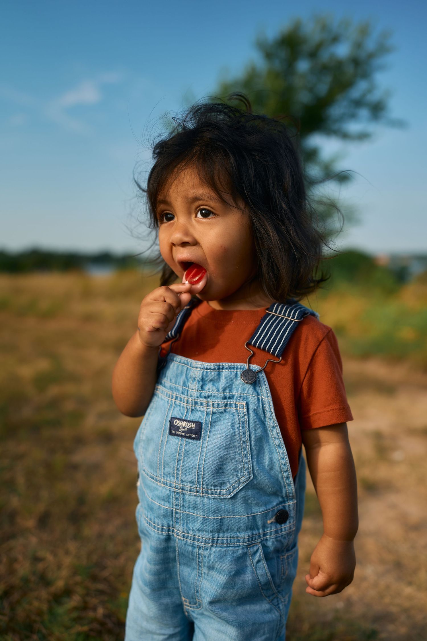 Young child in denim overalls and rust colored shirt playing outdoors.