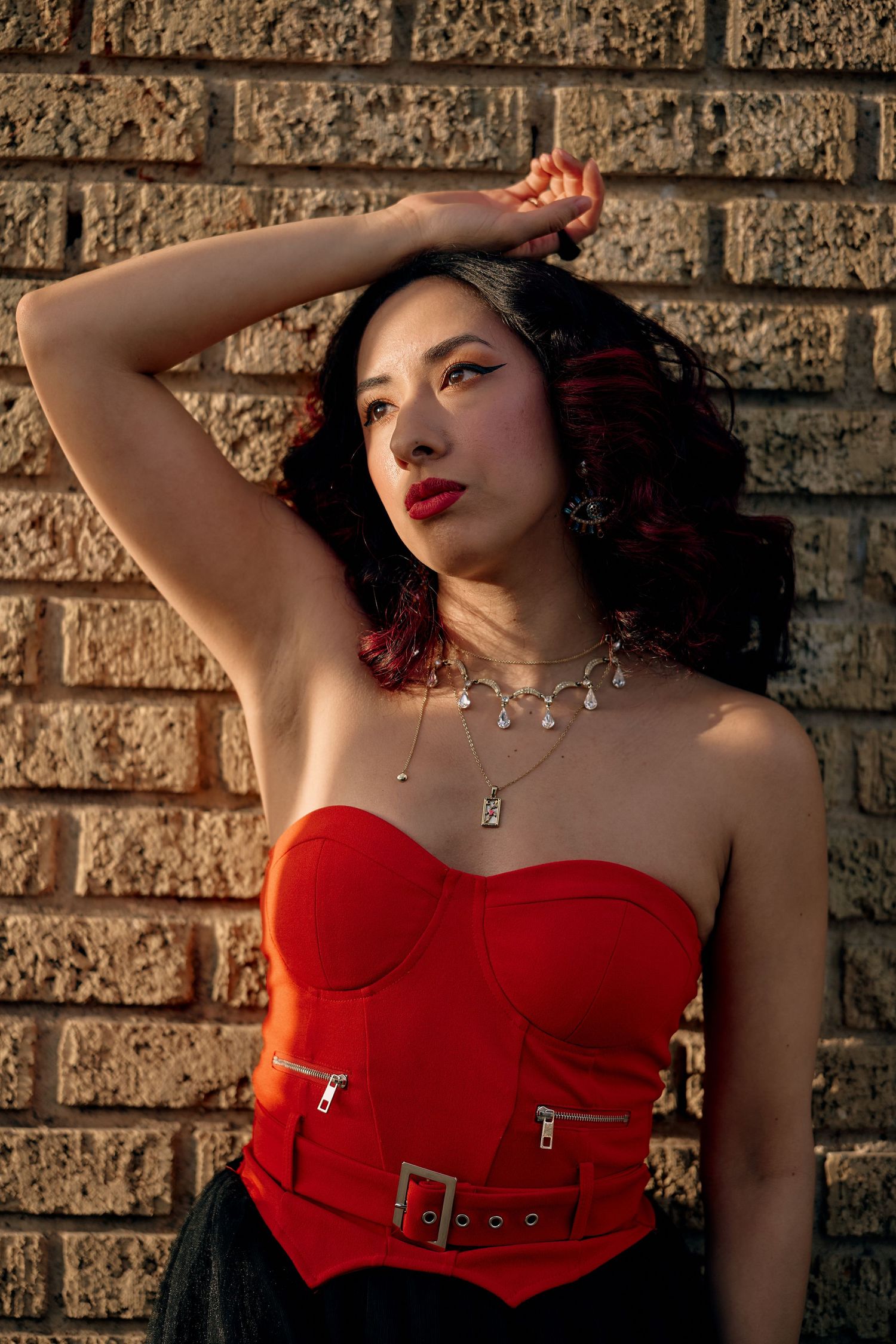 A series of four artistic fashion photos featuring a red corset top against a textured stone wall backdrop.