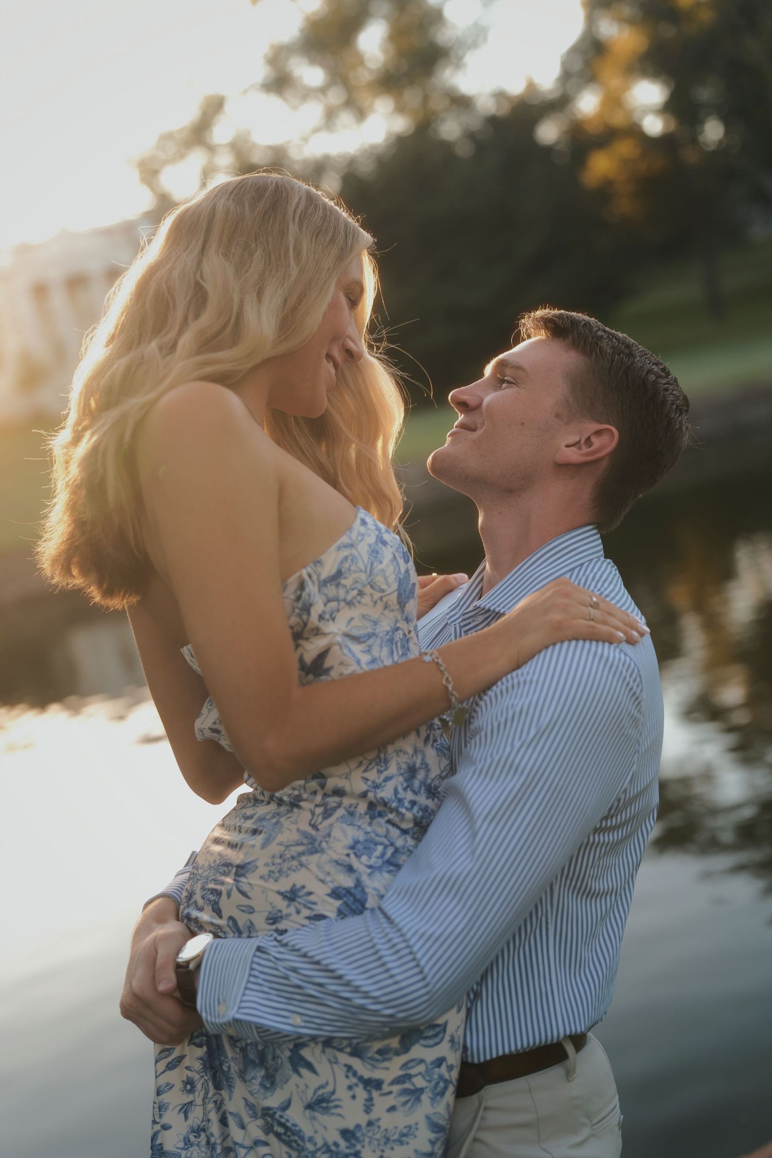 Couple shares intimate embrace by lake during golden hour sunset.