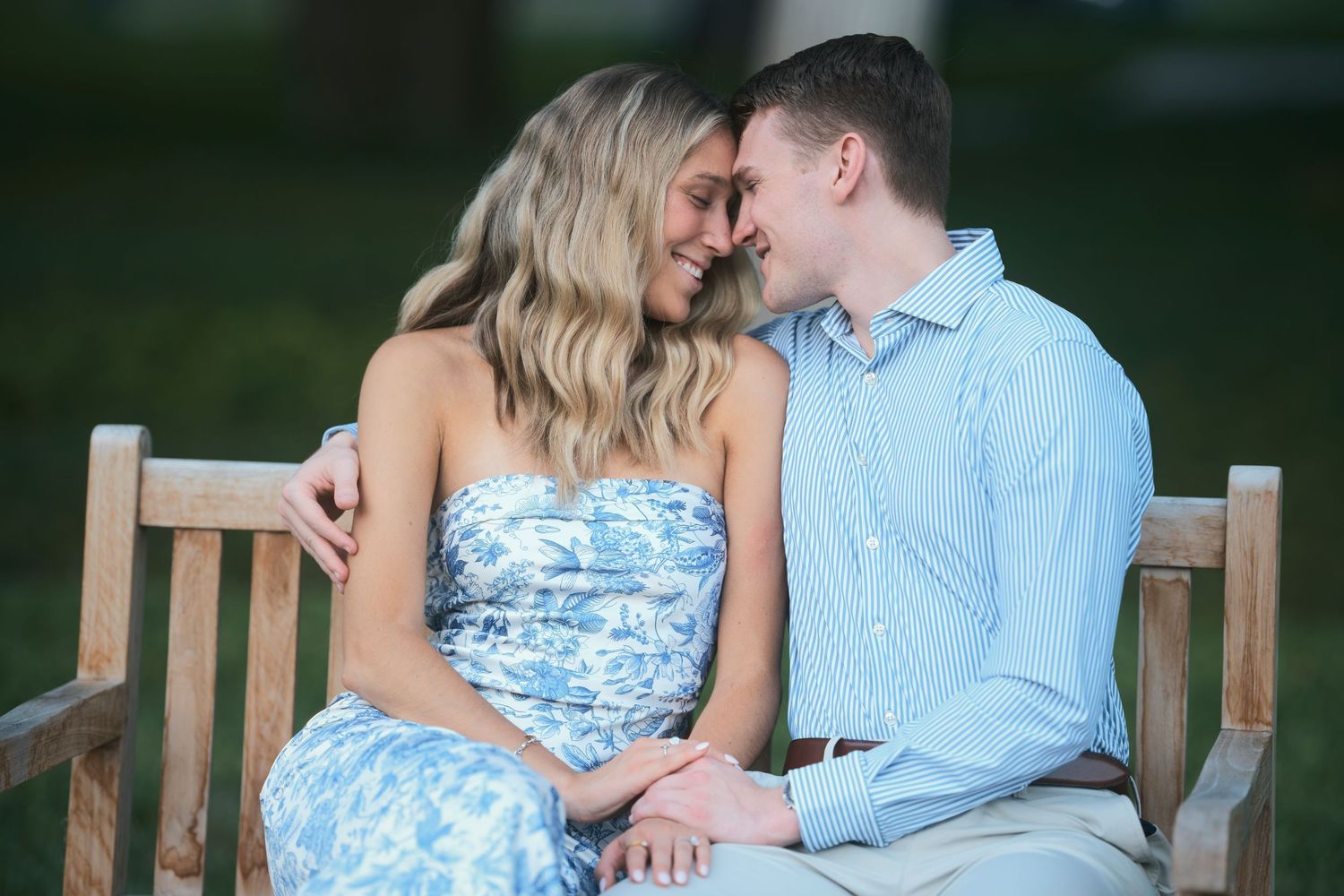 Romantic couple in coordinating blue outfits share an intimate moment while sitting together on wooden bench outdoors.