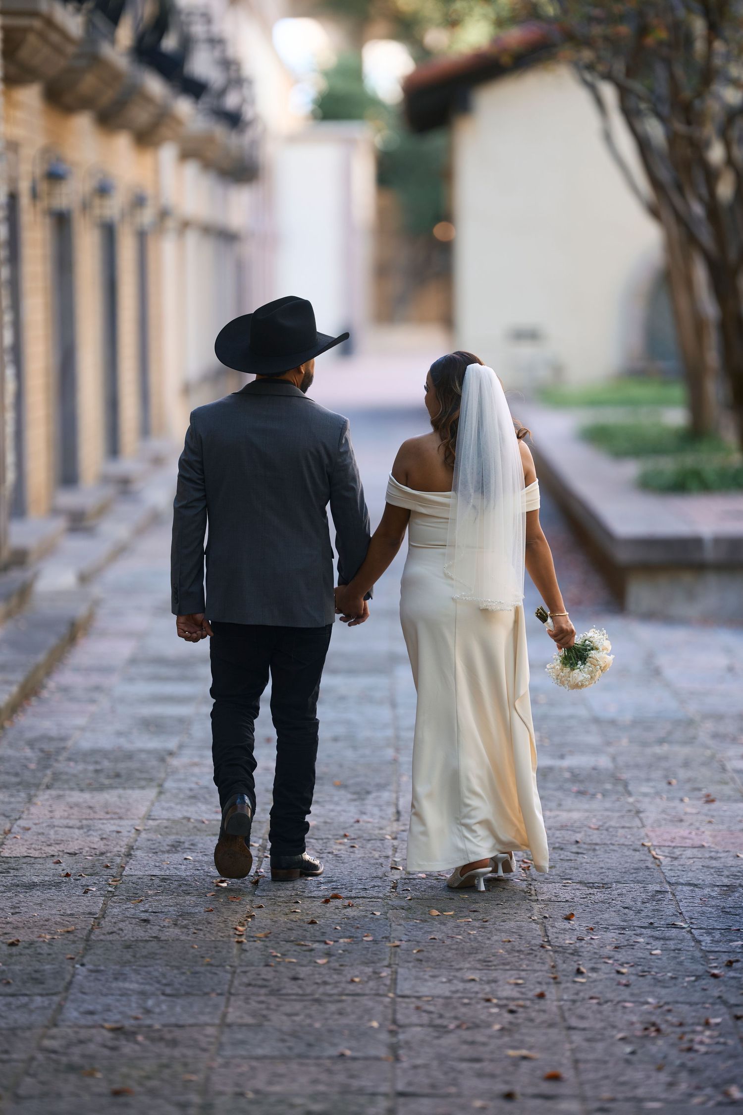 Wedding couple walking together down stone pathway in formal attire.