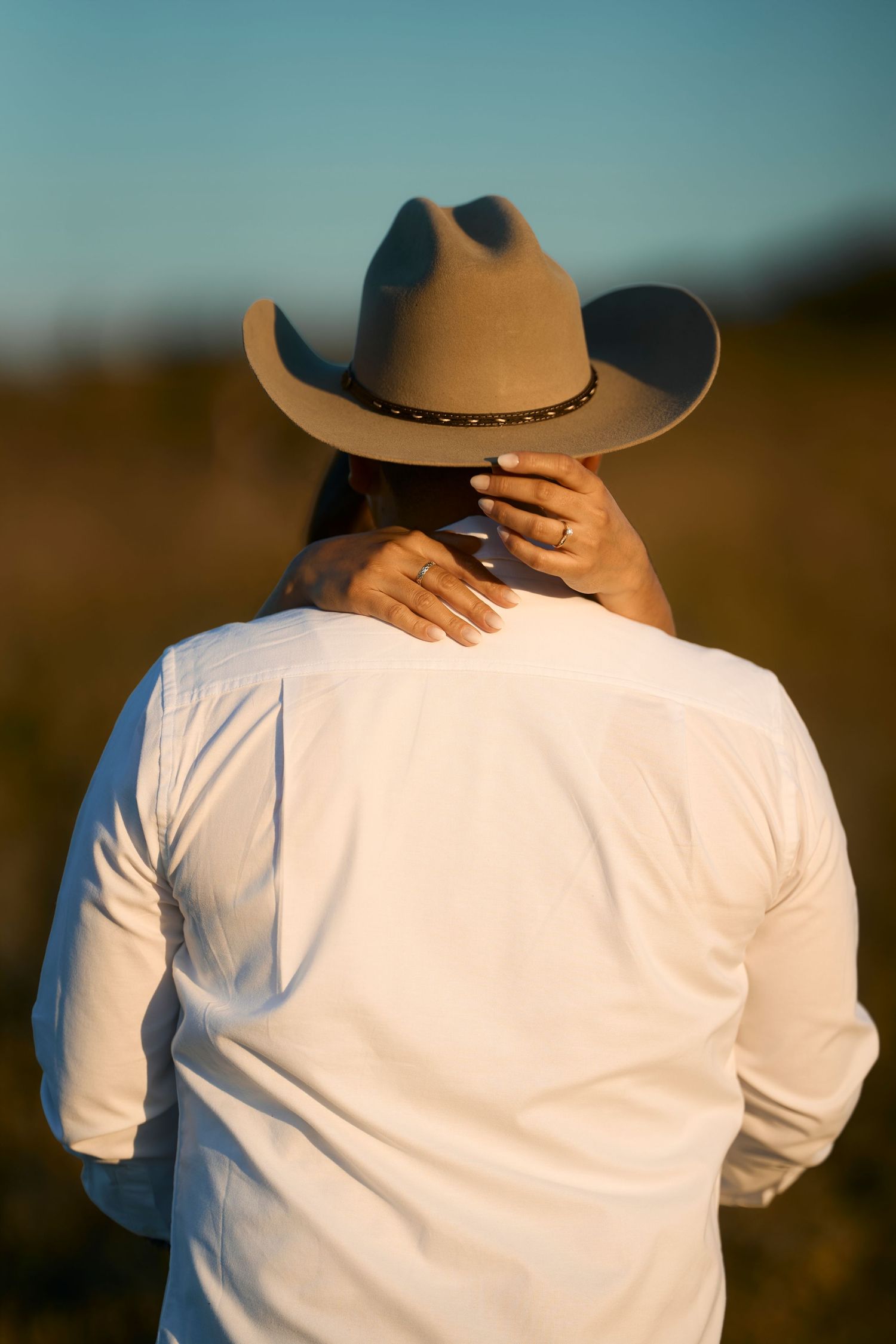 Person wearing white shirt and cowboy hat photographed from behind at sunset.