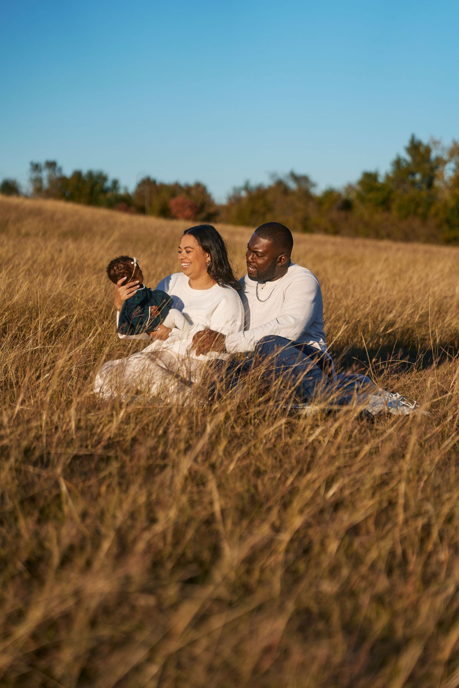 Couple relaxes in golden autumn field with their dog on a sunny afternoon.