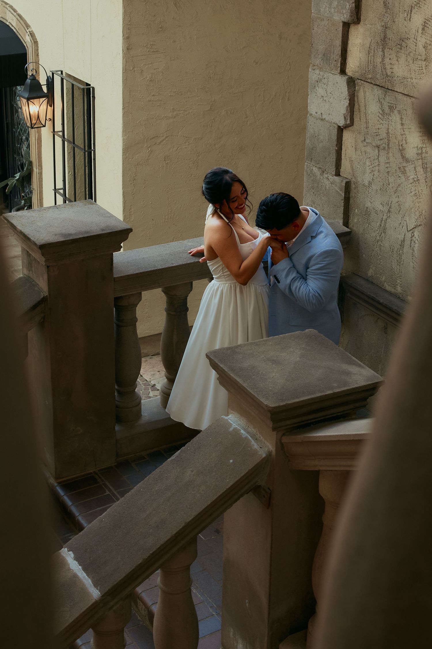 A couple shares a romantic kiss on a stone staircase in what appears to be a European architectural setting.