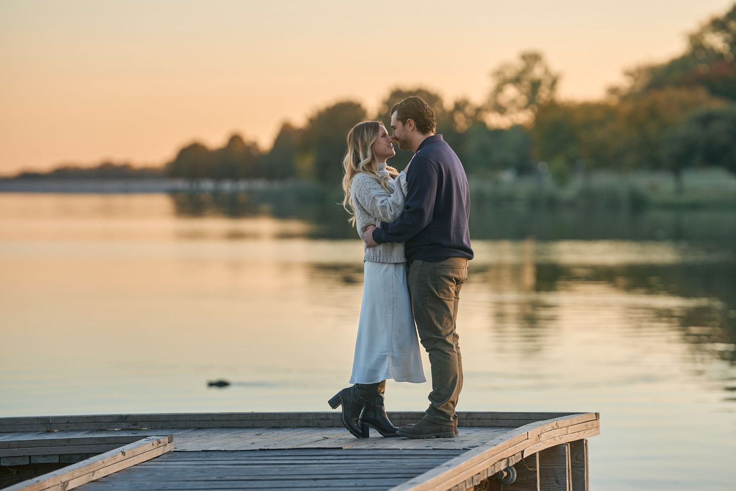 Romantic couple embracing on wooden dock during golden sunset over lake.