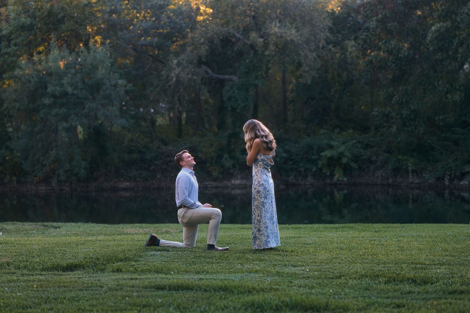 People gathered in a grassy field during sunset with trees in background.