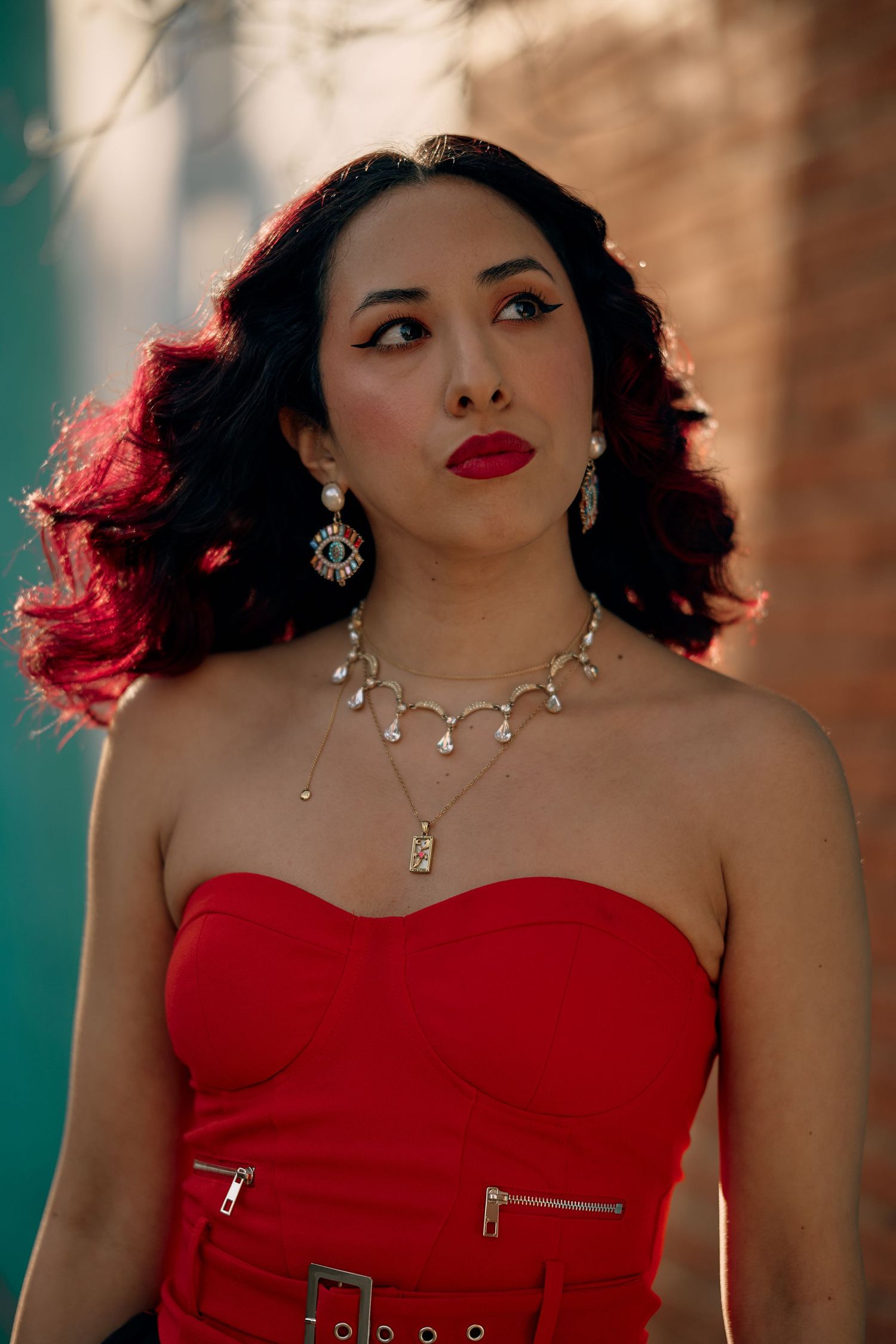 A glamorous portrait series featuring a woman in a red strapless dress with statement jewelry against a teal background.