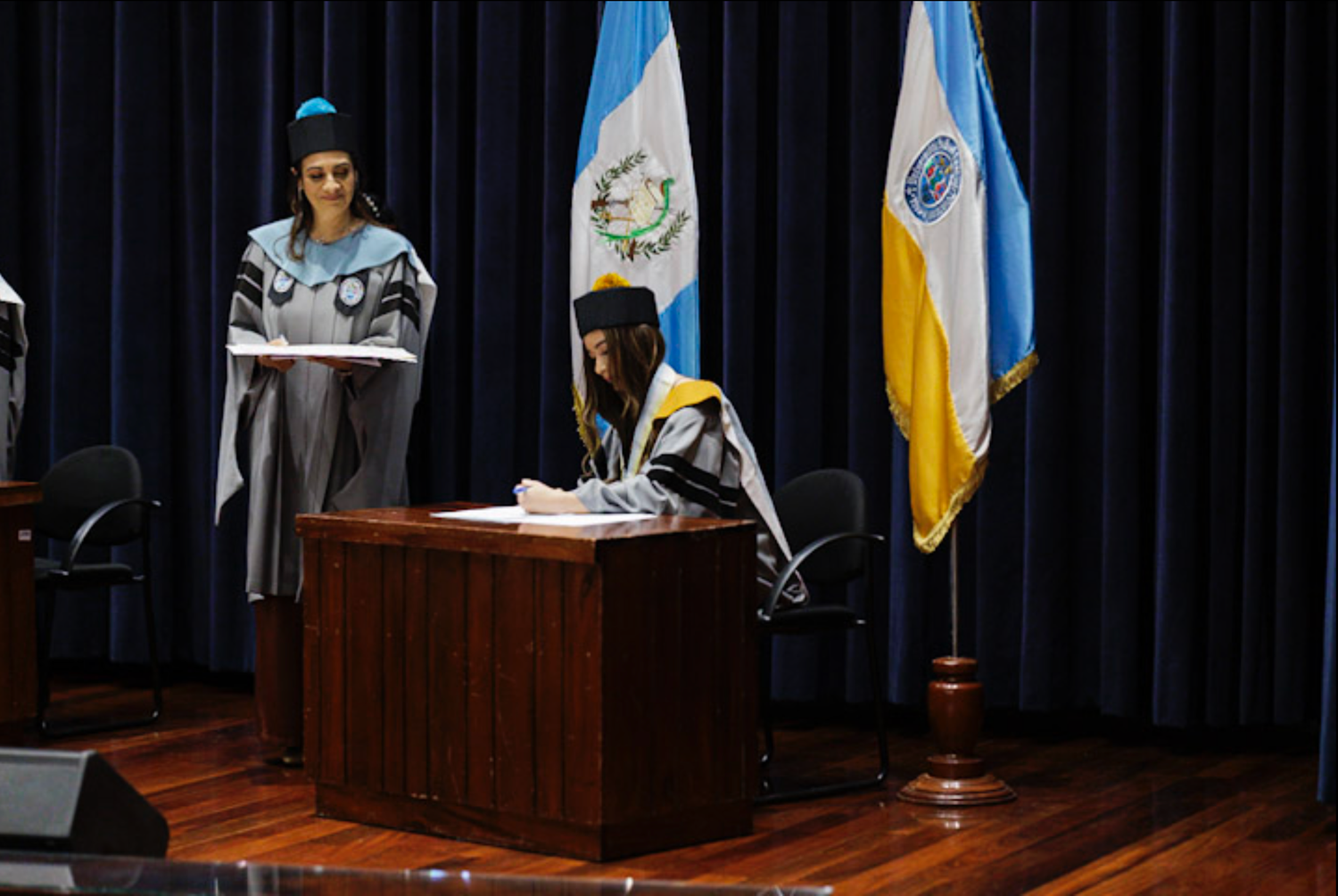 Academic ceremony with flags of Guatemala and Argentina on stage.
