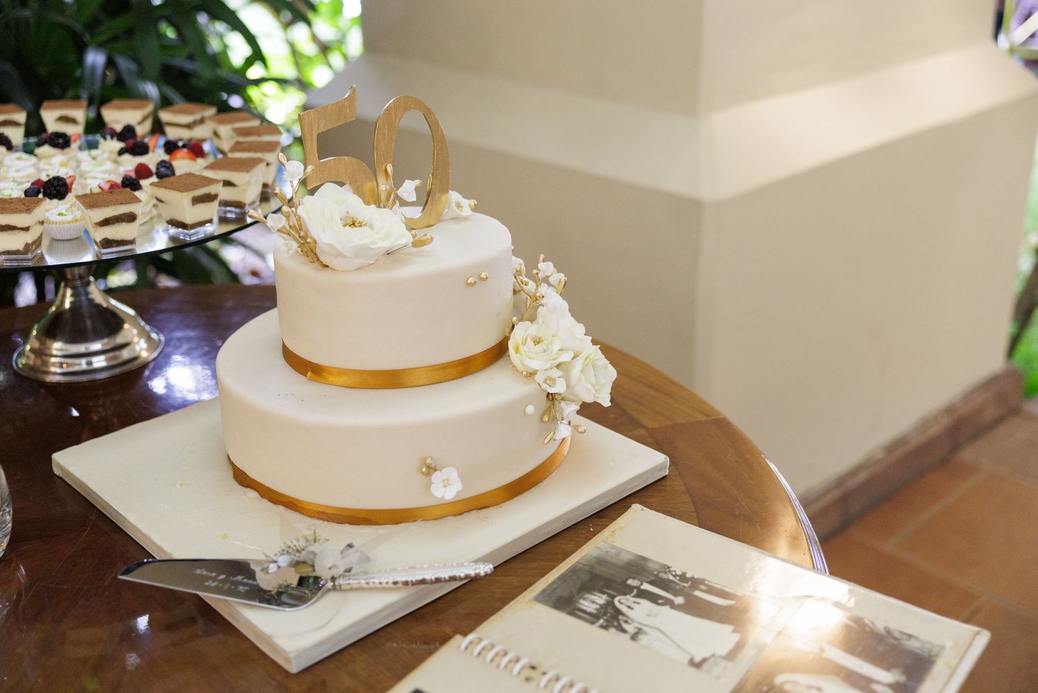 White wedding cake with gold ribbon trim displayed on a table.
