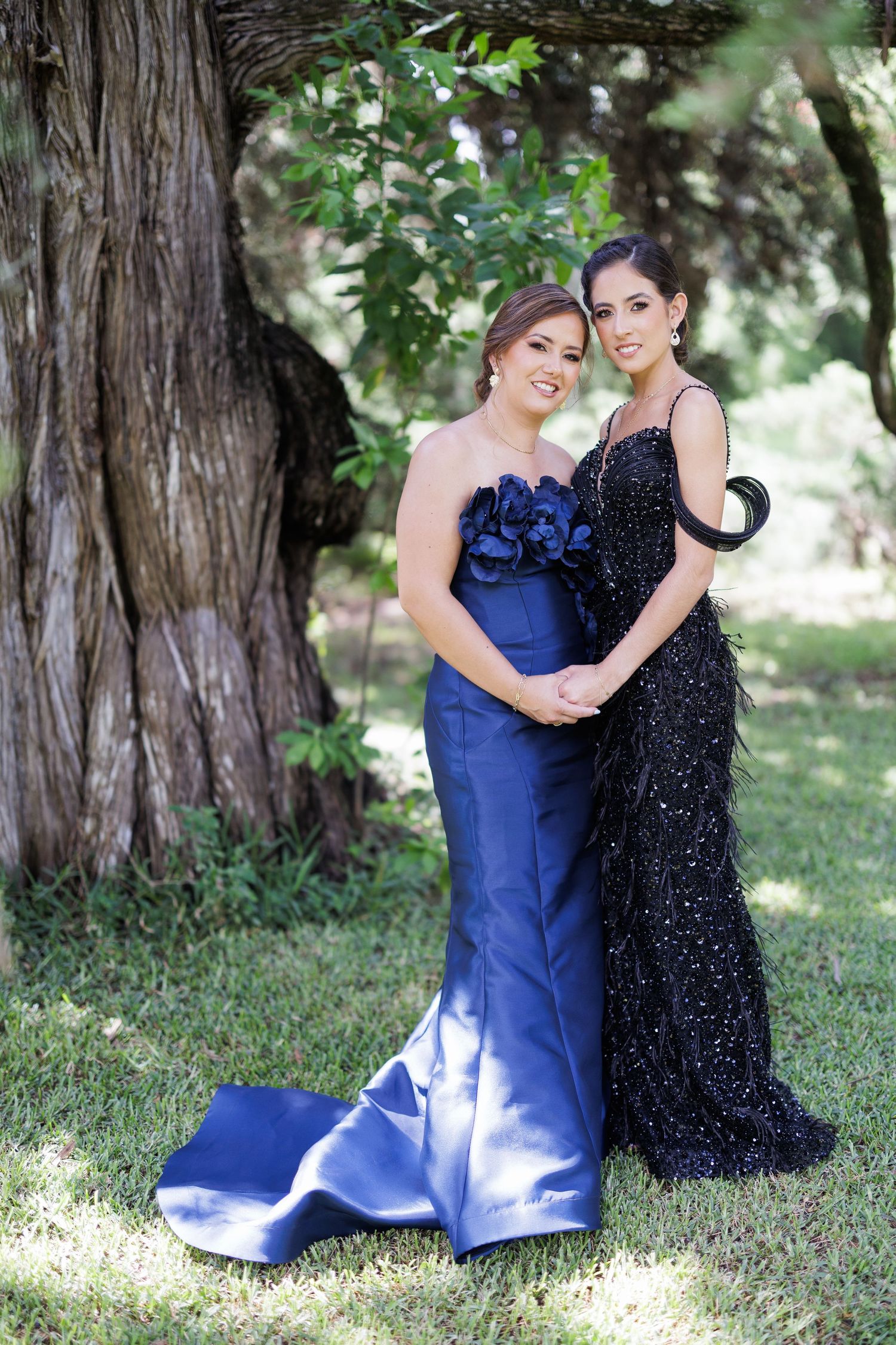 Two people in contrasting blue and black formal dresses share a tender moment outdoors.
