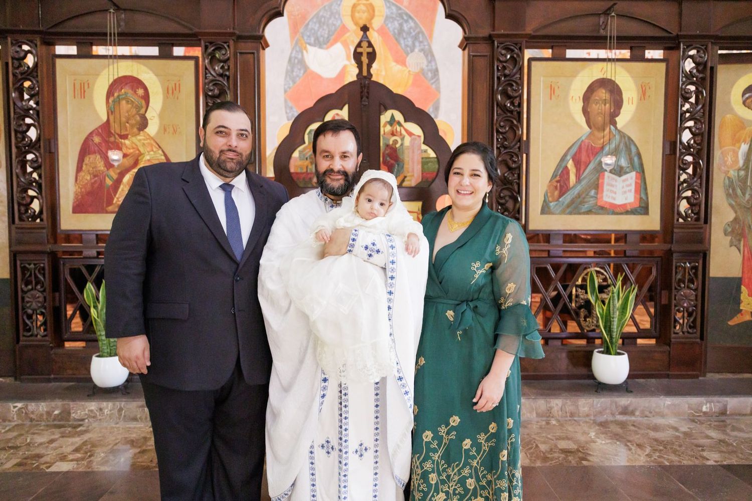 Family group photo at Orthodox church baptism ceremony with religious icons.