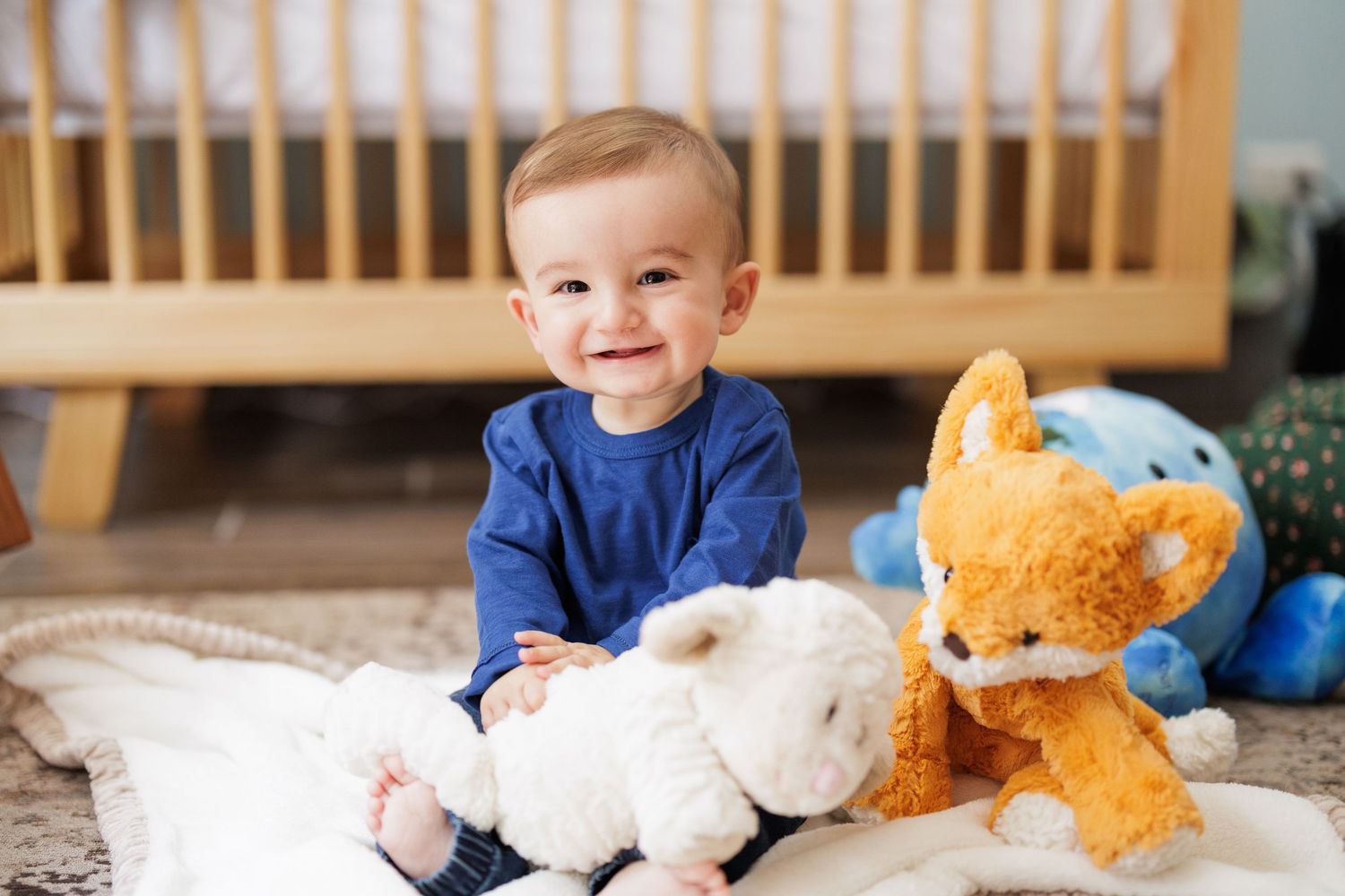 Baby in blue playing with stuffed animals on a wooden bench.