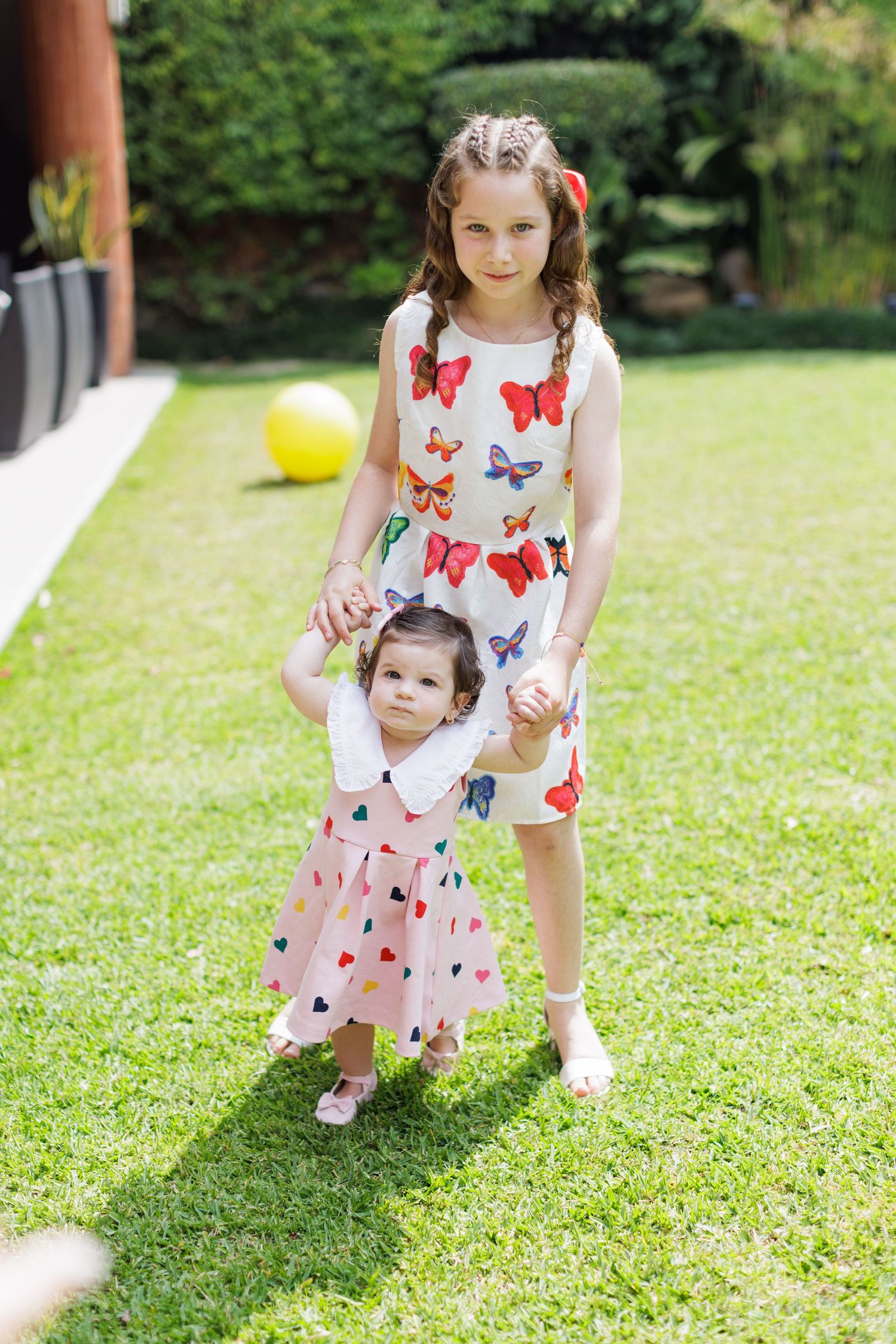 Two people in butterfly print dresses standing on green lawn.