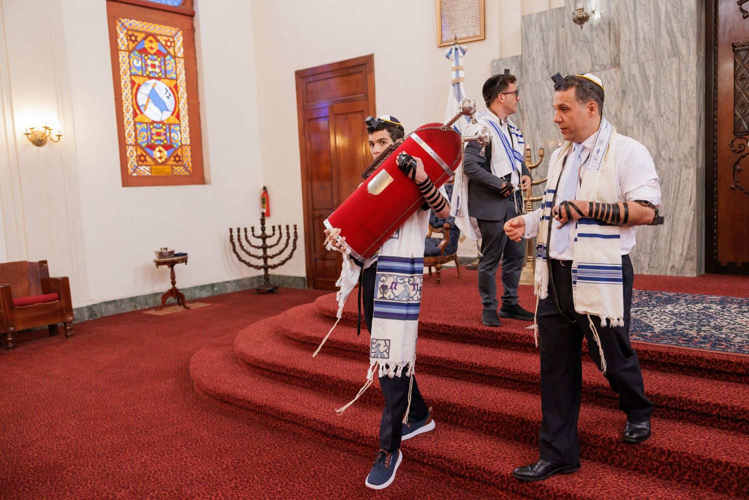 Joyful celebration inside a synagogue with people dancing and carrying ceremonial items.