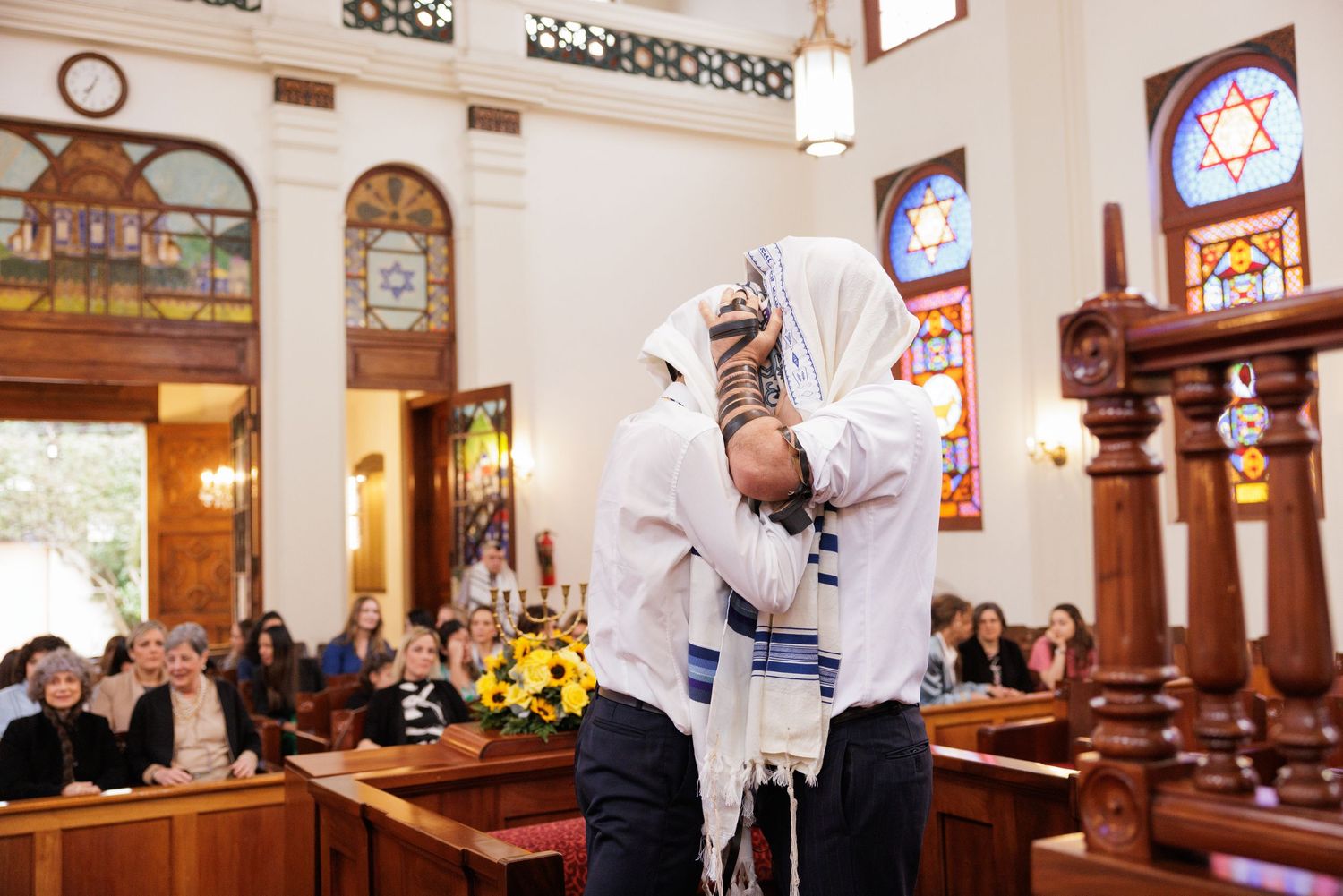 Congregation gathered in a synagogue with traditional Jewish symbols and decorative windows visible.
