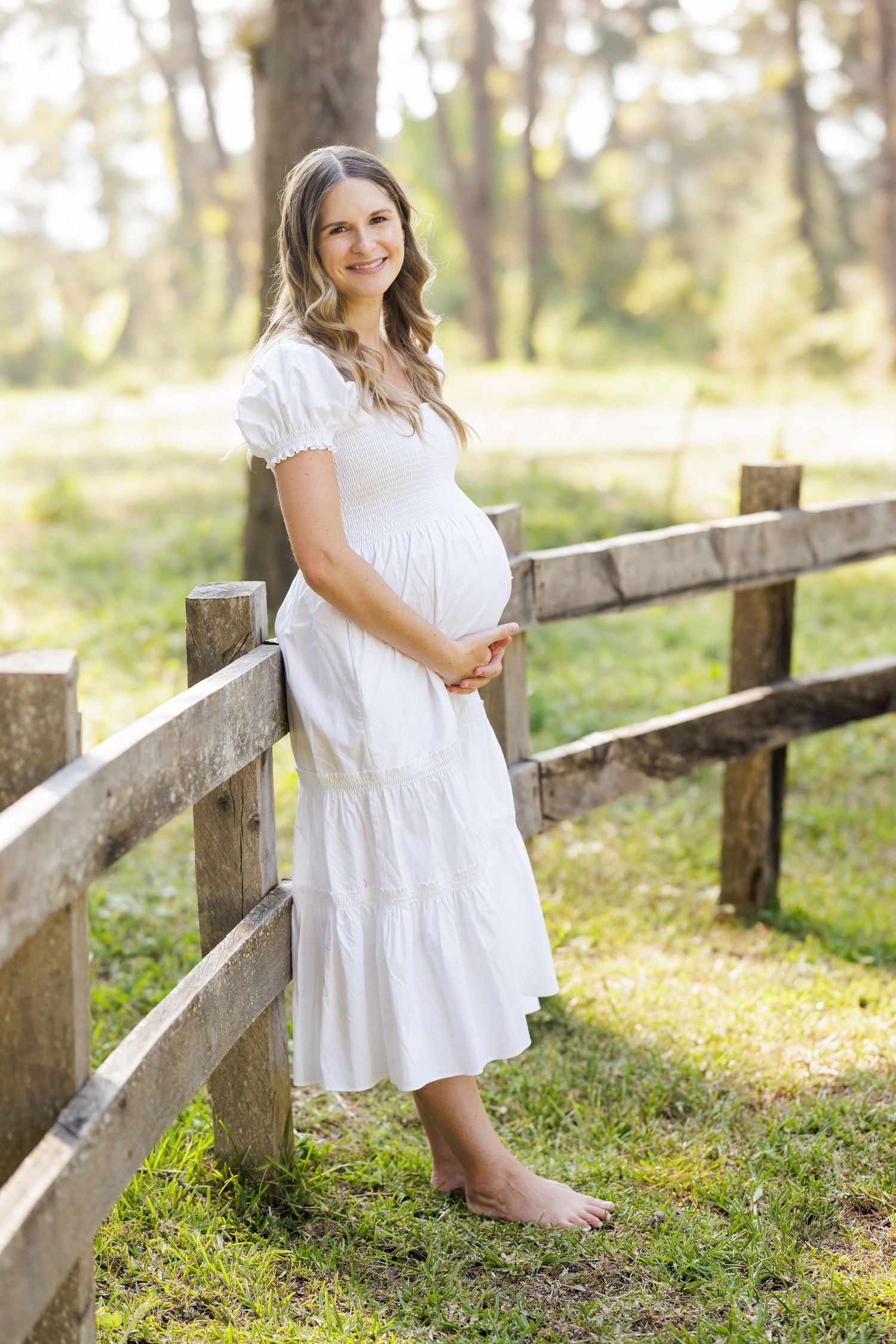 A flowing white dress contrasts beautifully with a rustic fence in dappled sunlight.