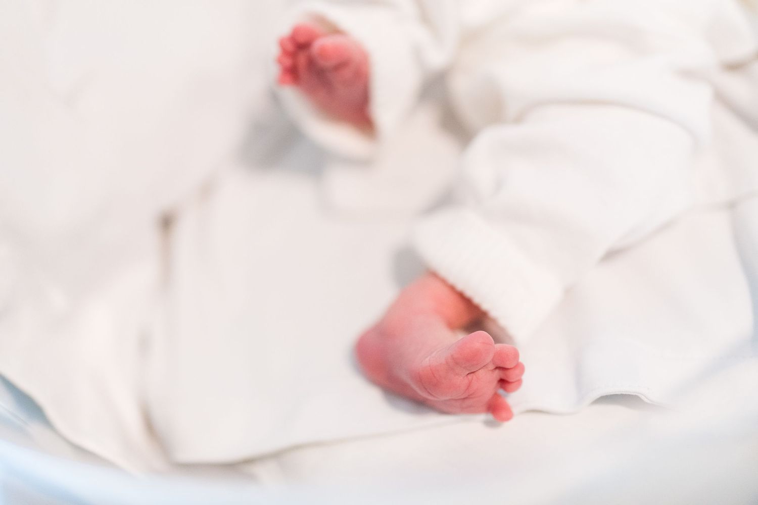 Close up detail of newborn baby's feet against white fabric.