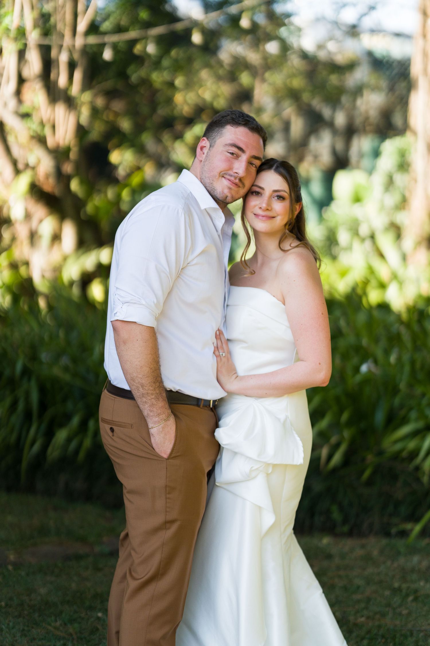 Newlyweds share intimate moments in a garden setting wearing white and brown attire.
