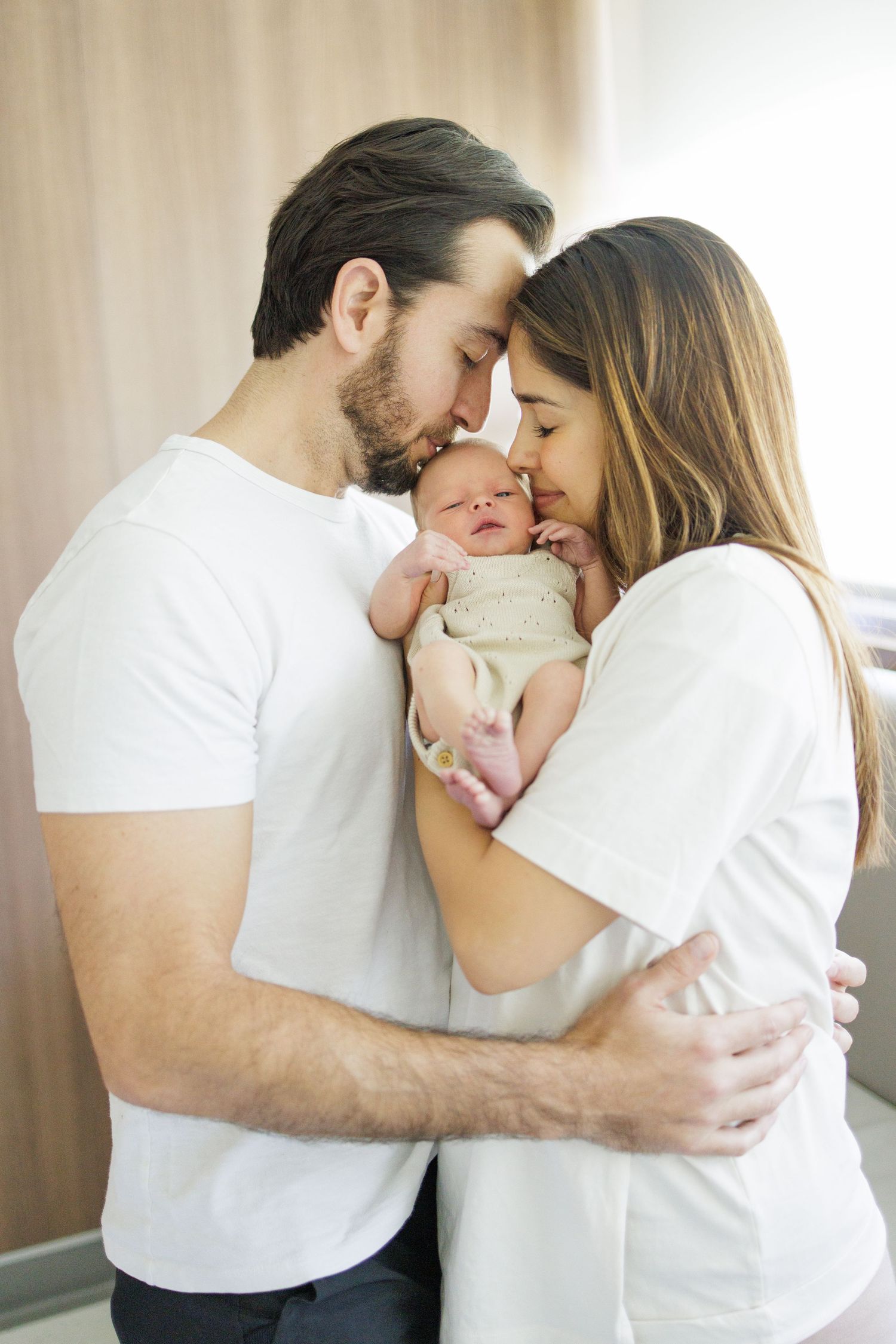 Family sharing tender moments with newborn baby in white decorated room.