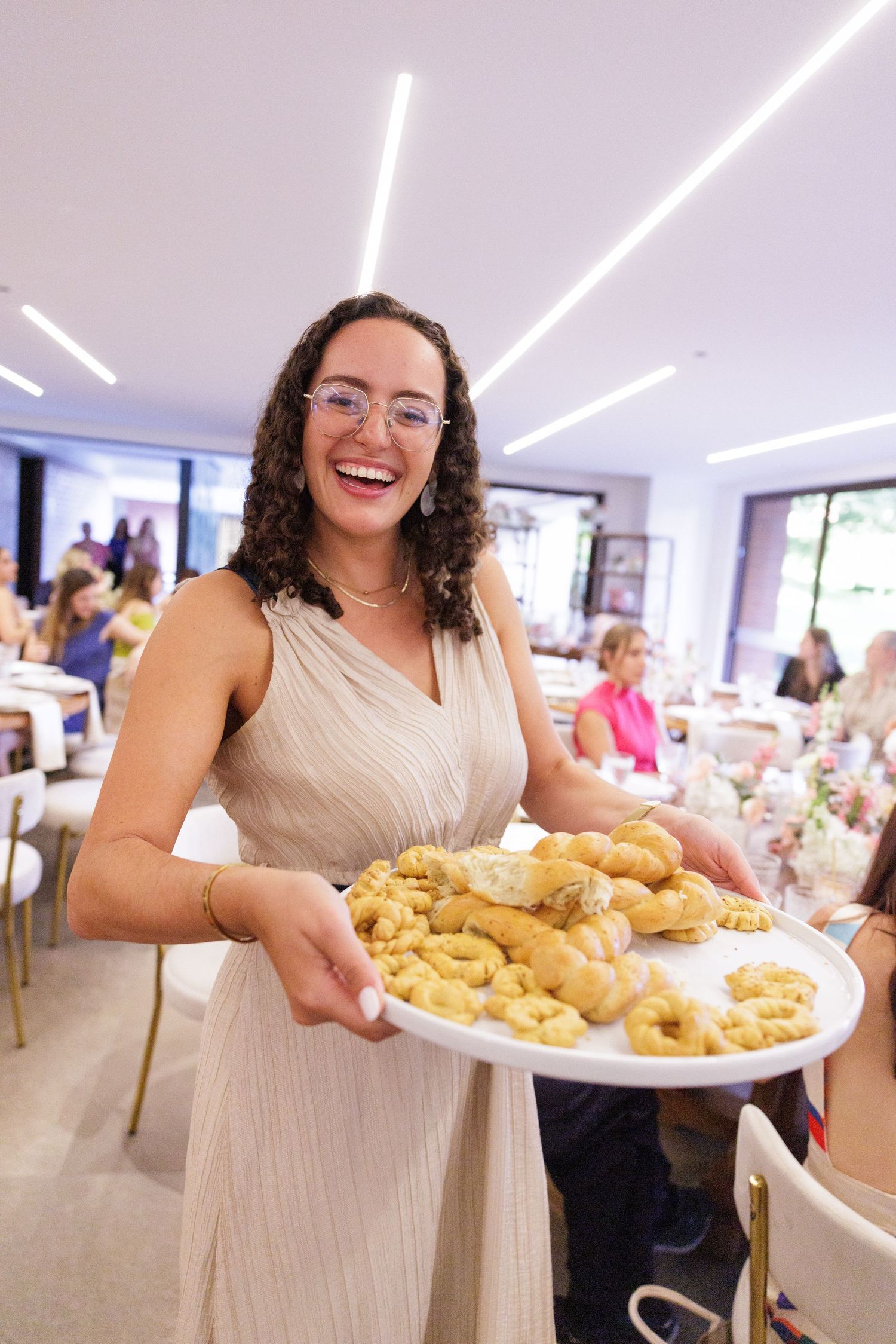 Person in cream-colored dress serves platters of golden pastries at an event.
