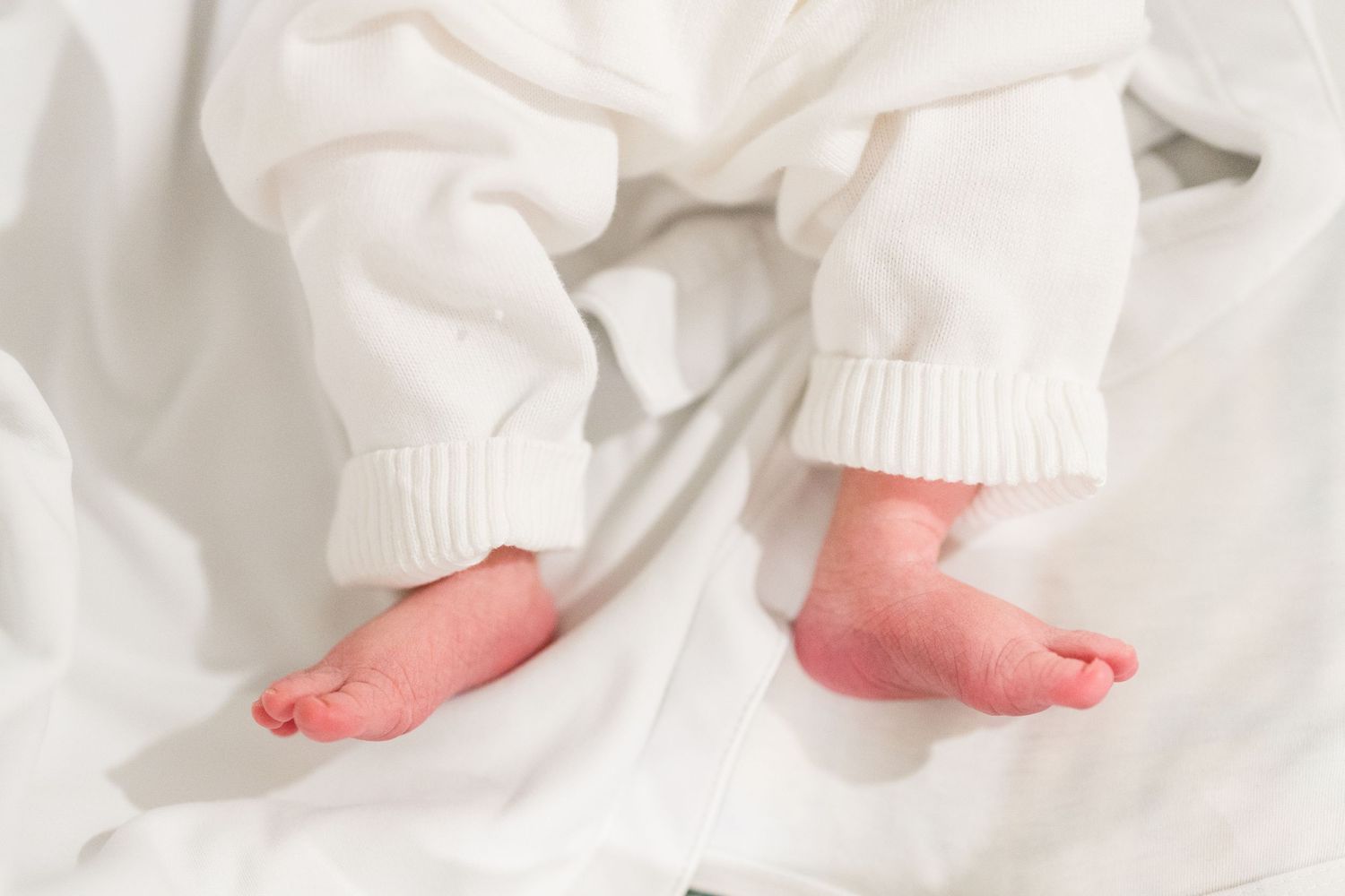 Close up of tiny newborn baby feet wrapped in white knit clothing.