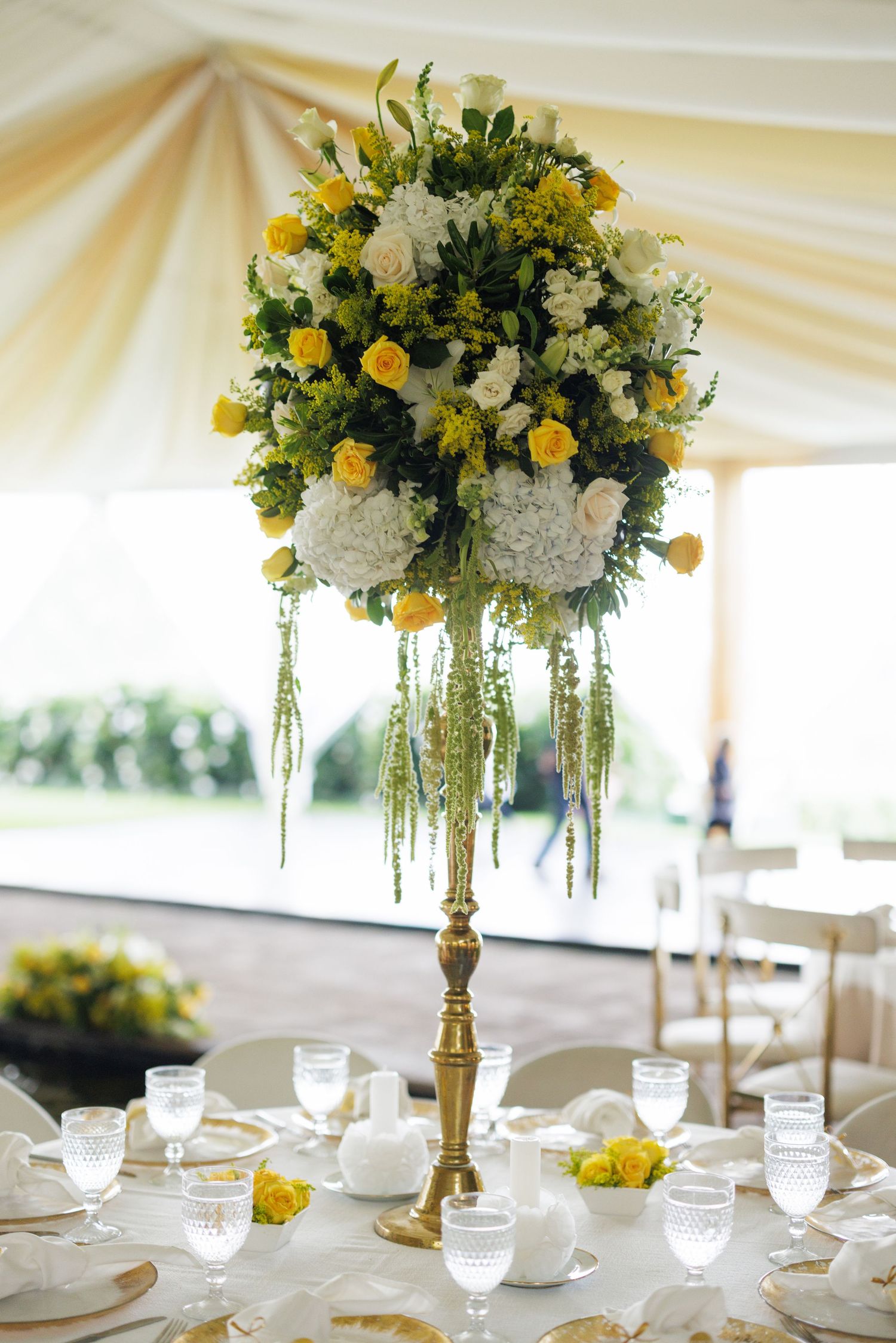 Elegant floral centerpieces with yellow roses and white flowers on reception tables.