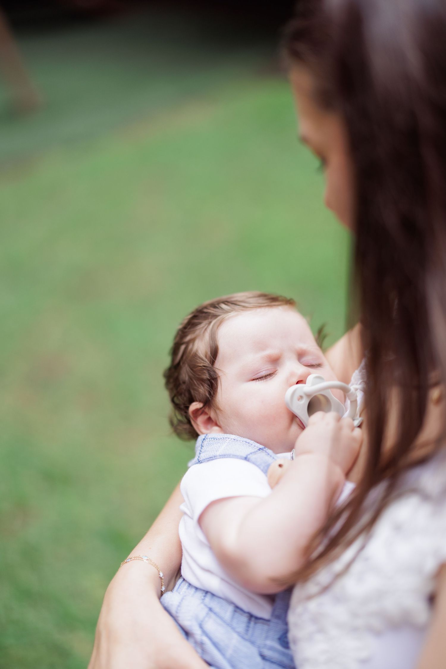 A tender moment captured as a baby drinks from a bottle outdoors on a grassy background.