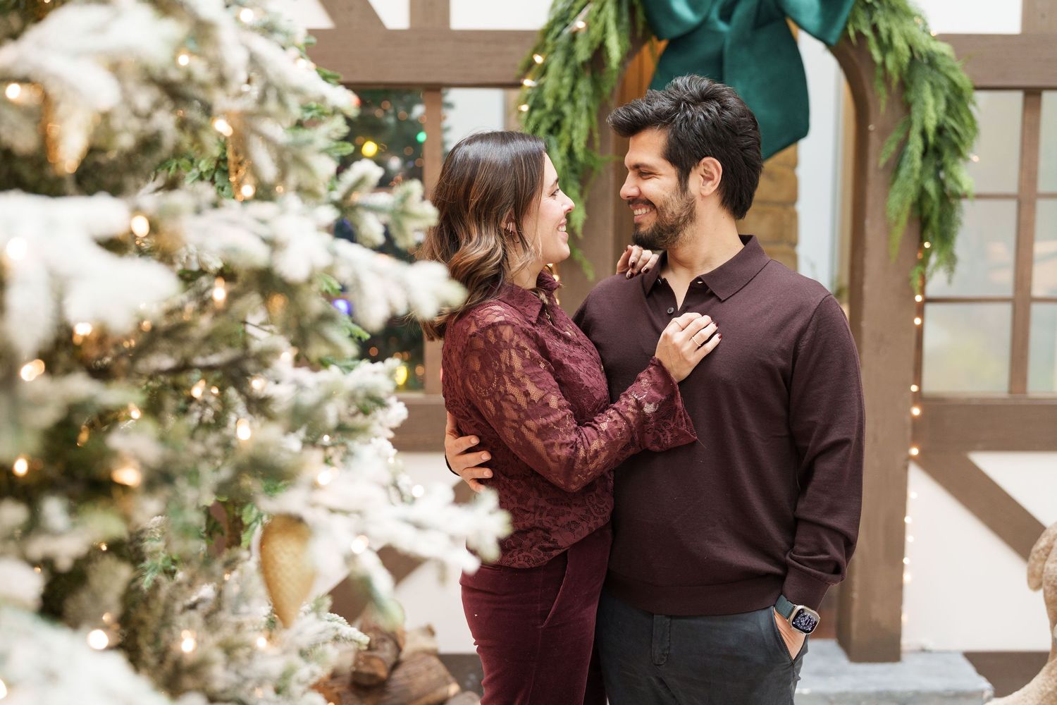 A couple shares an intimate moment in front of a decorated Christmas tree.