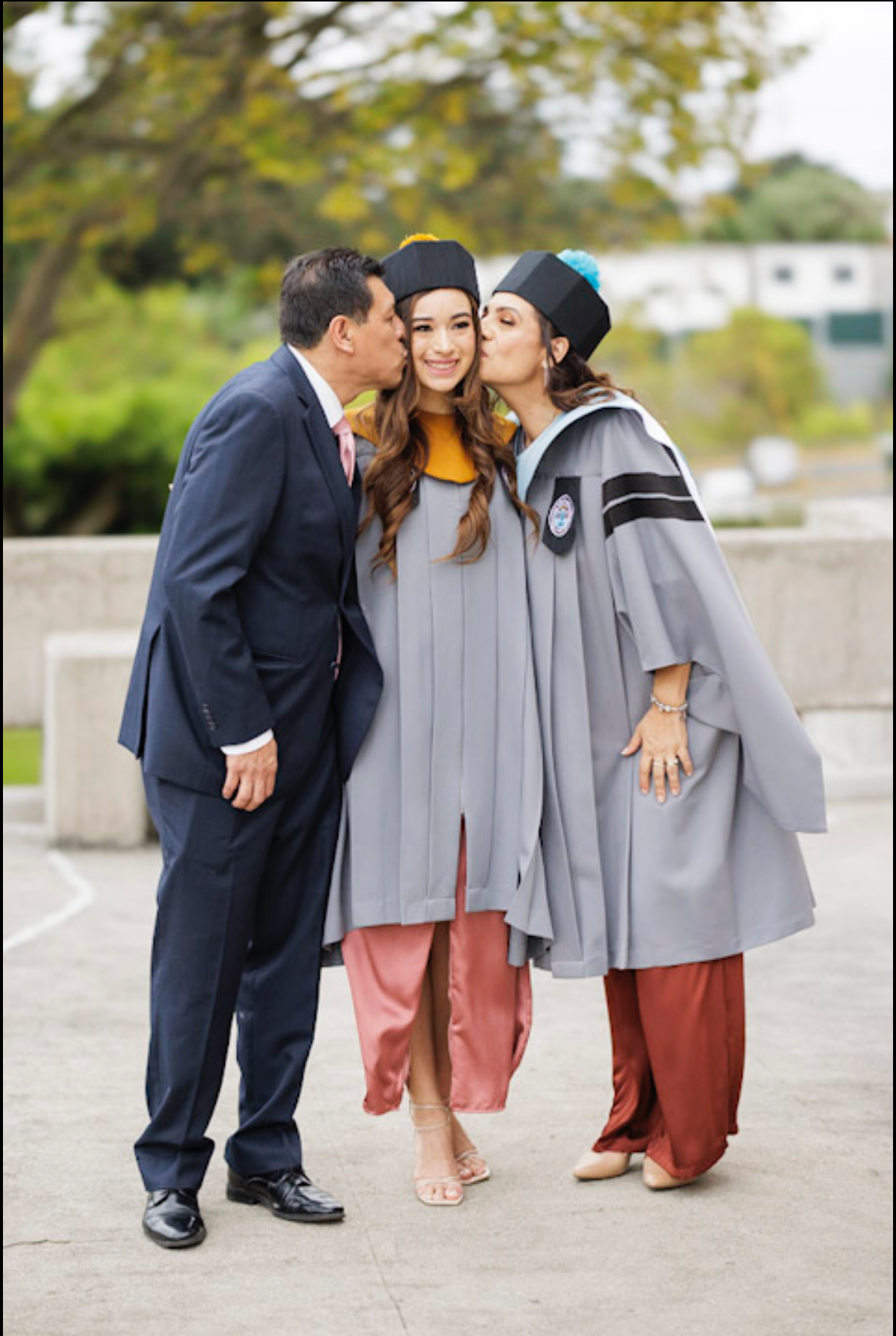 Three people in graduation attire sharing a celebratory moment with kisses on the cheek.
