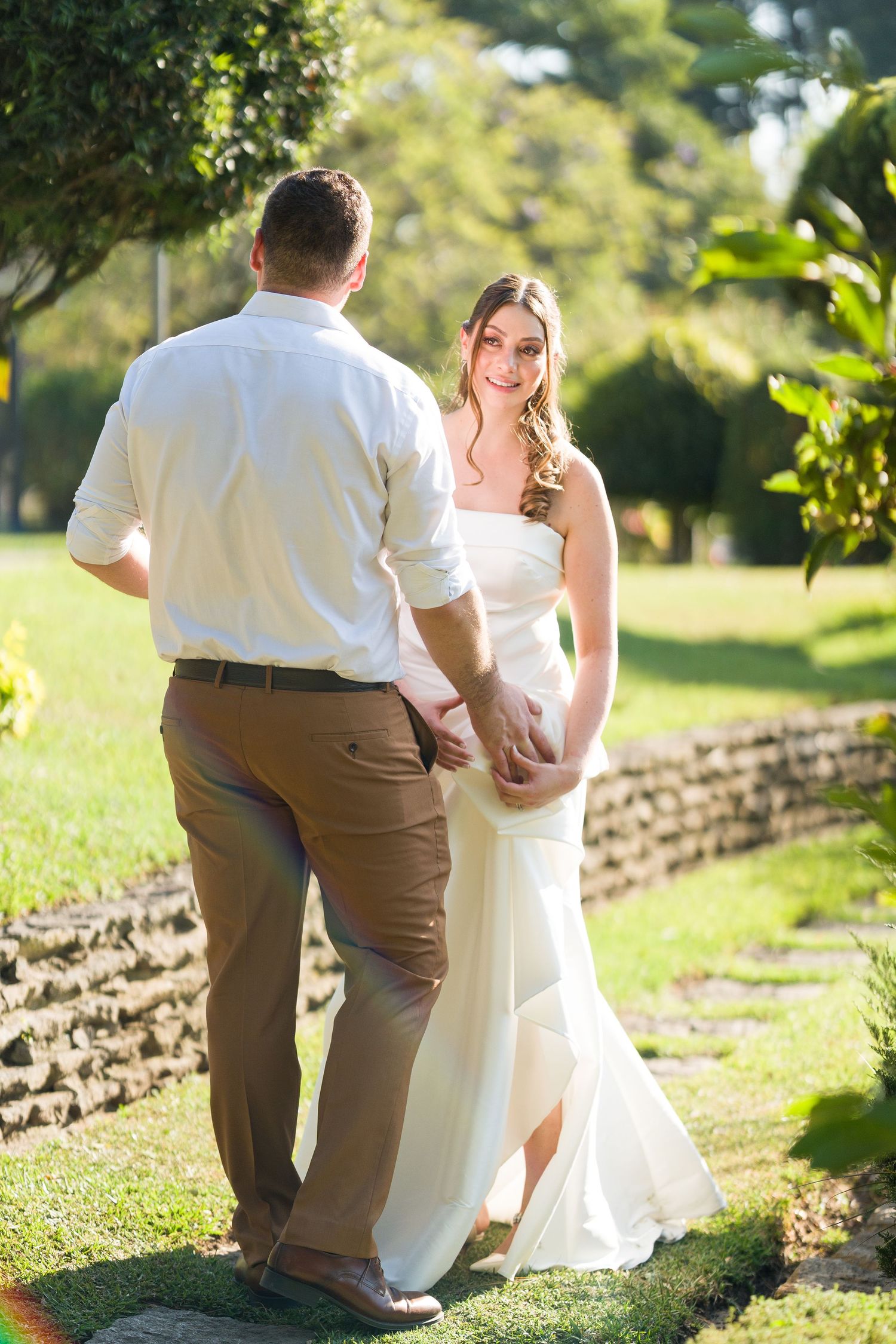 Wedding couple poses together in a sunlit garden setting.