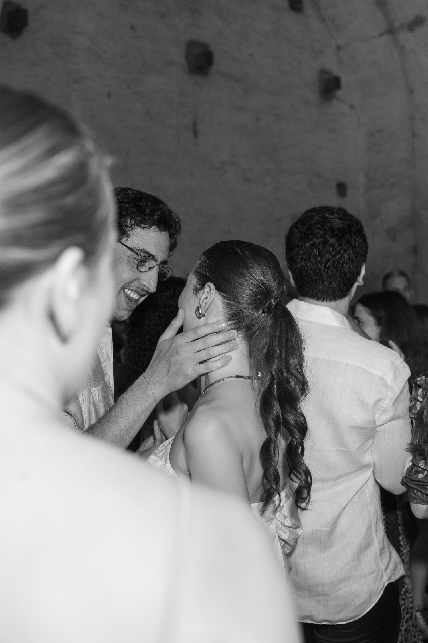 Black and white candid photo of guests sharing an intimate moment at a wedding celebration.