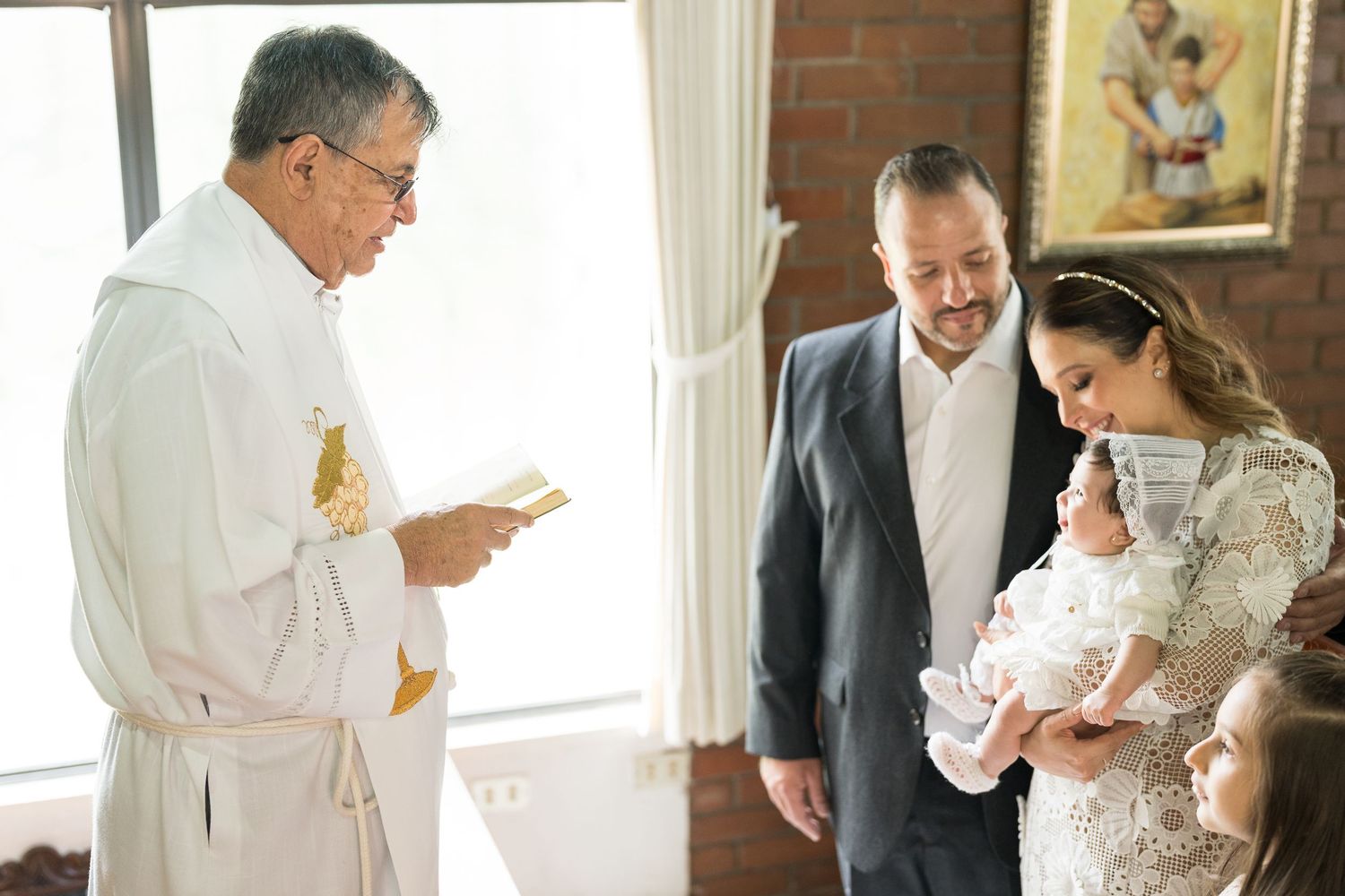Baptism ceremony in progress with white baptismal gown and religious officials.