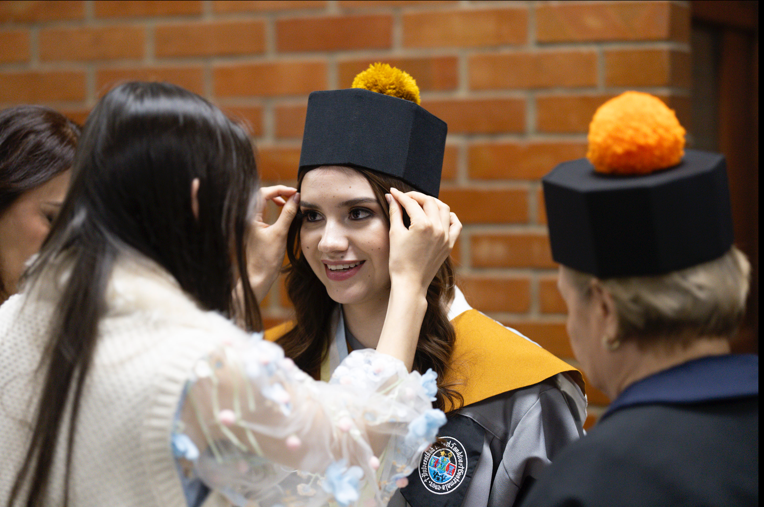 Graduate getting help adjusting cap before ceremony while others look on.