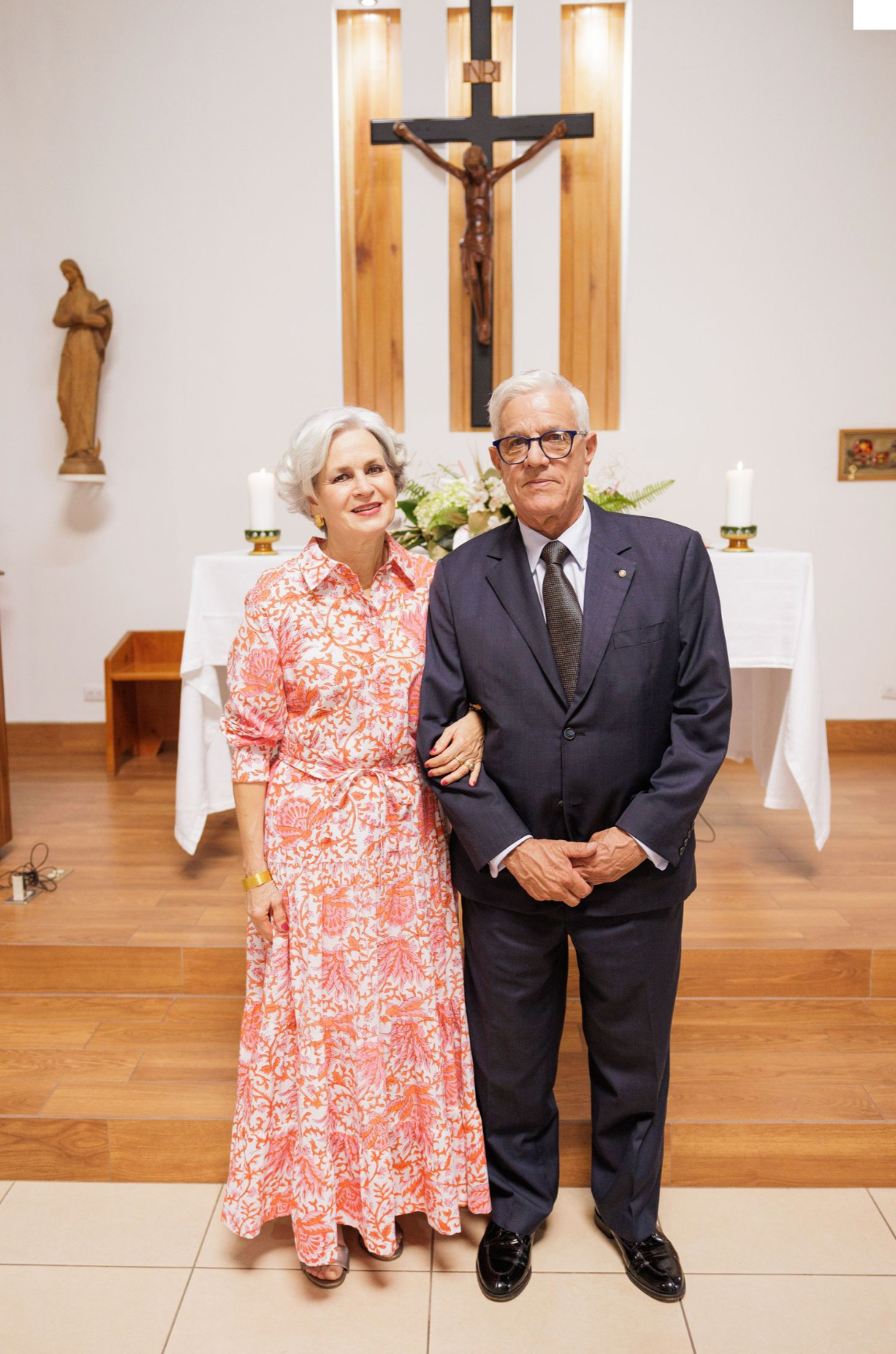 Elderly couple poses in church with crucifix and altar in background.