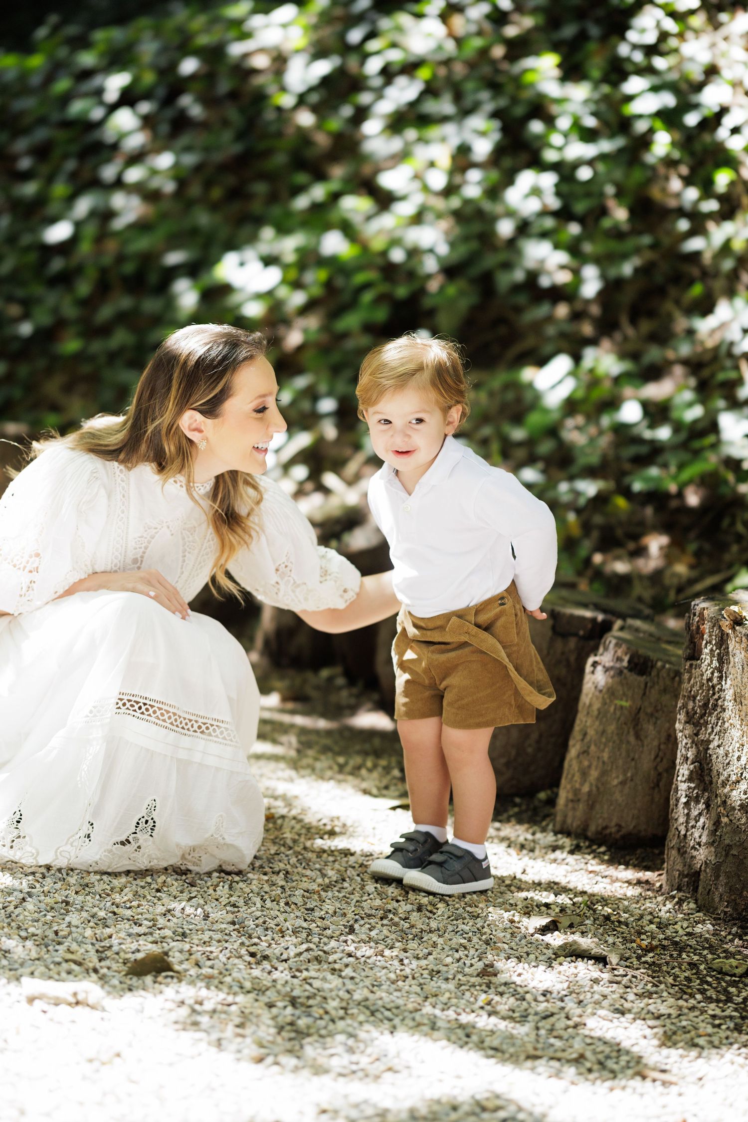 Playful outdoor family photography session under dappled tree shade on white gravel ground.