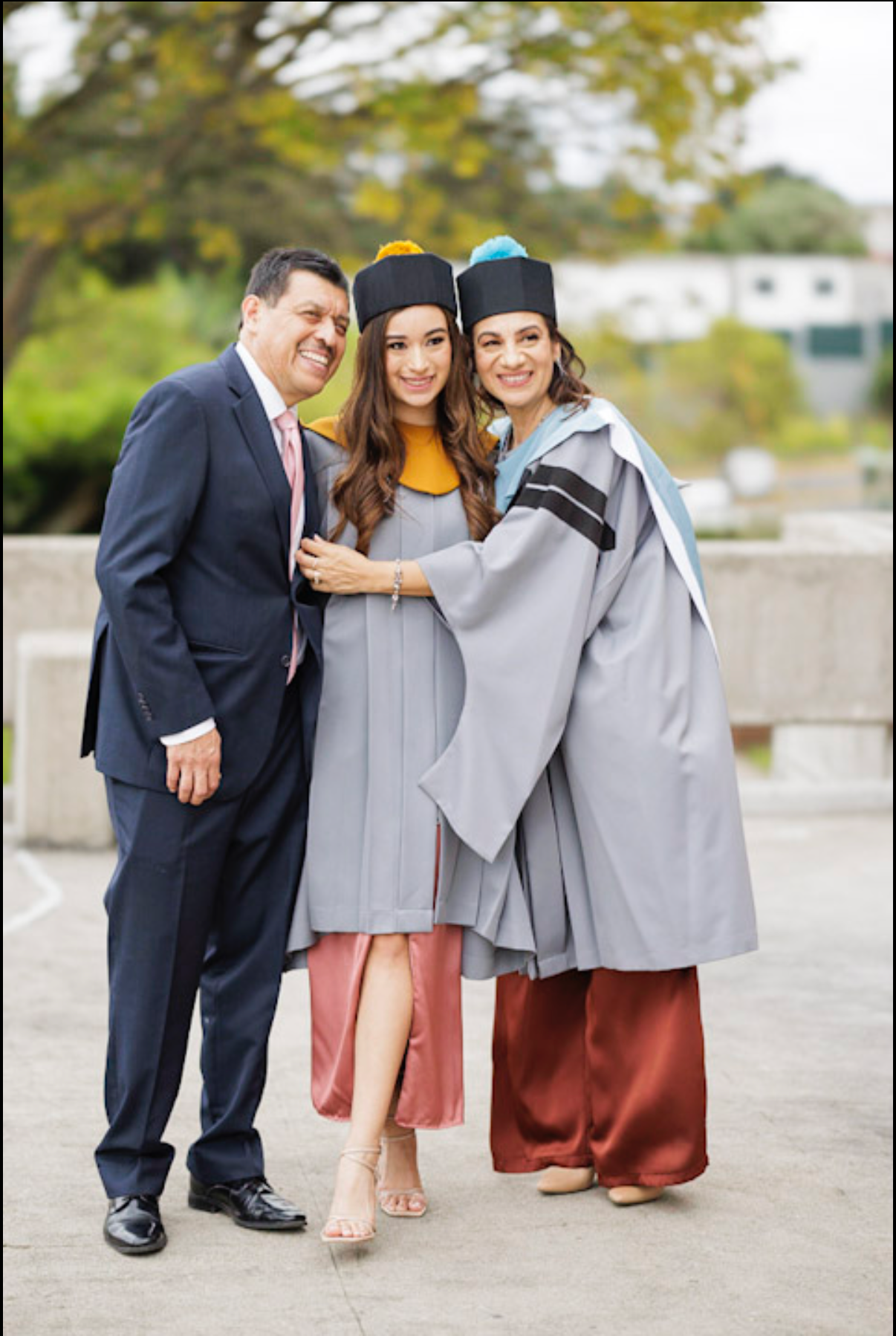 Family graduation photo with multiple graduates in grey robes posing together outdoors.