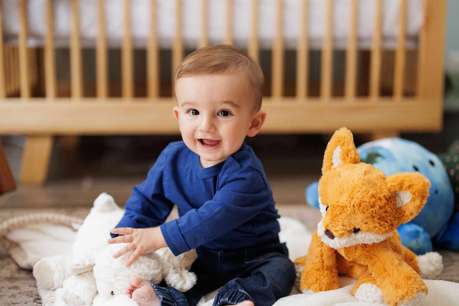 Toddler smiling while playing with plush toys on a wooden bench.