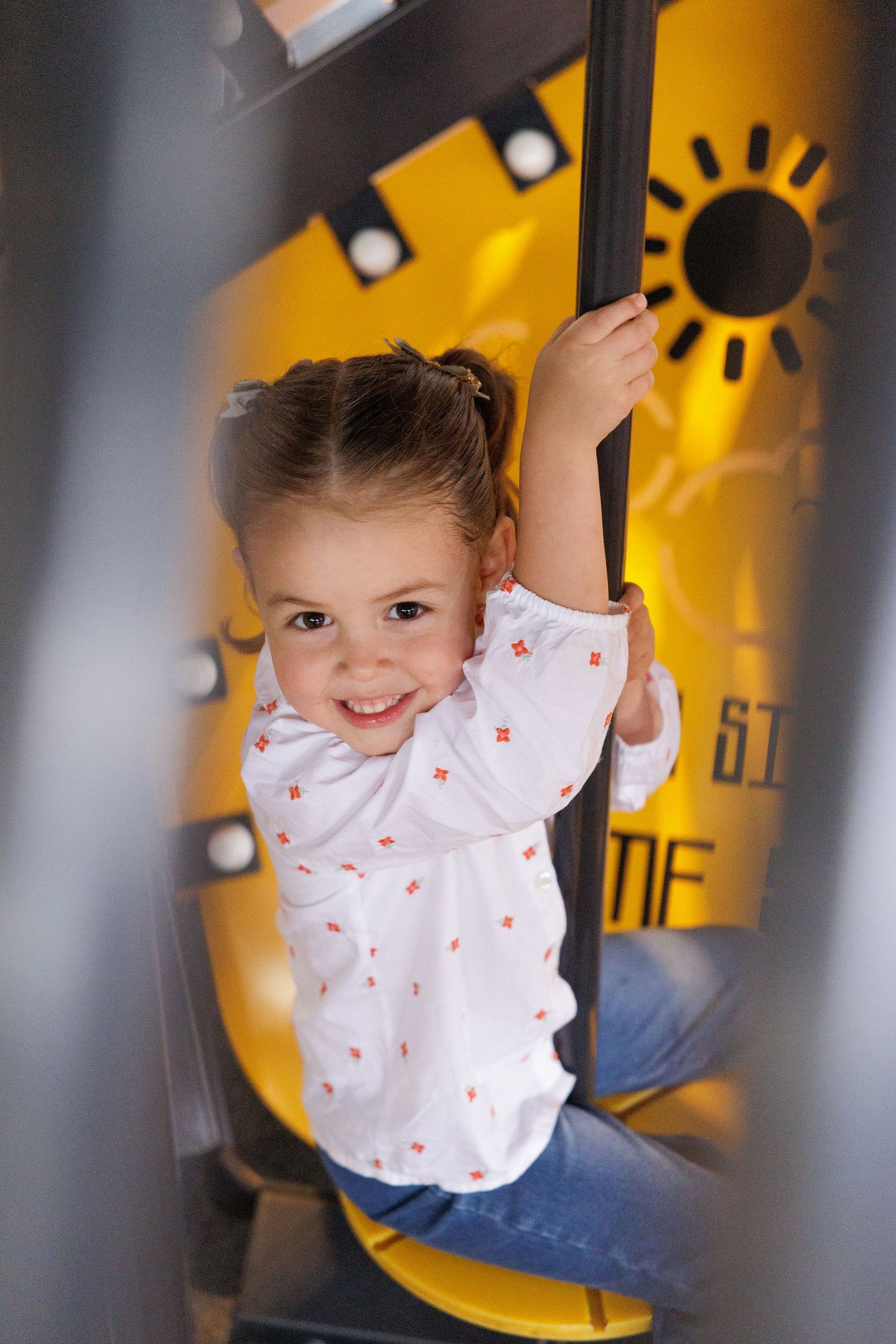 A playful moment captured on playground equipment with yellow background and sun artwork.