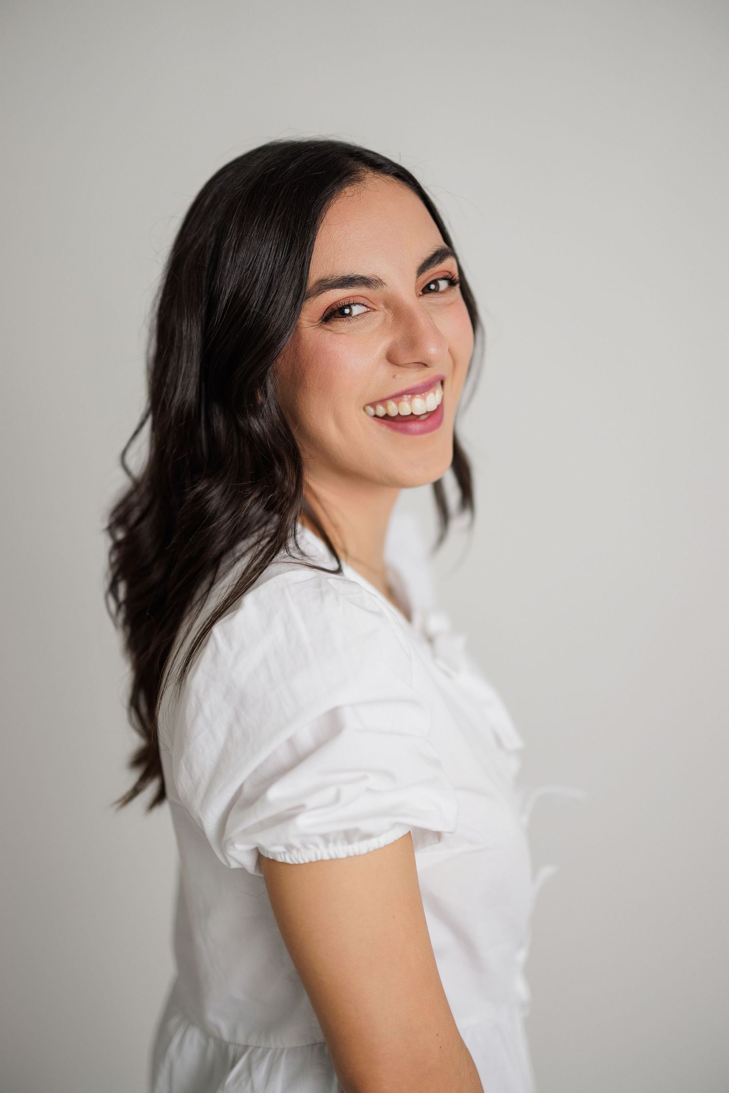 Professional studio portraits showing joyful expressions in a white top against a light gray background.