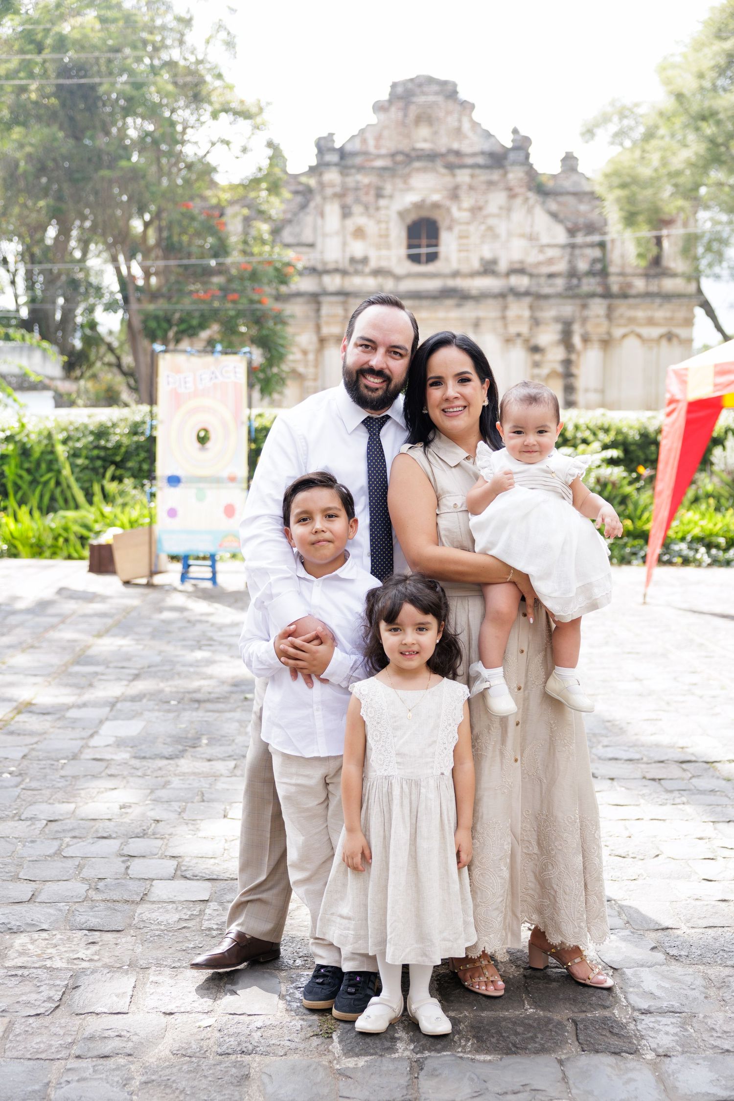 Family dressed in white and beige poses together in front of historic stone church.